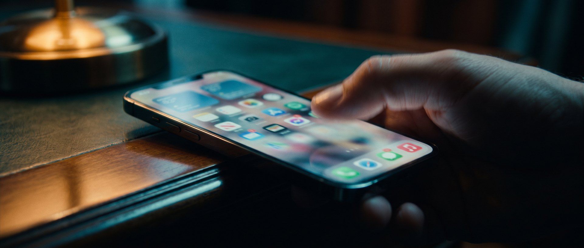 A hand resting on a lit smartphone on a dark desk, the screen glowing