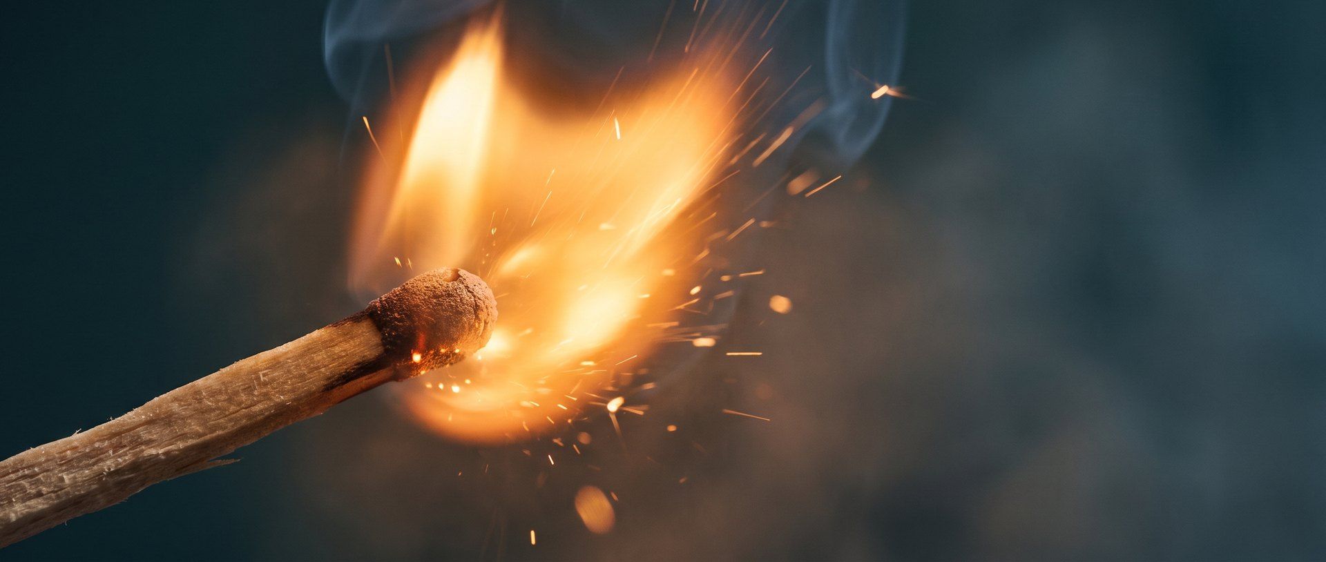 A single wooden match striking into a bright amber flame in the dark -- the spark of an idea AI can't copy.