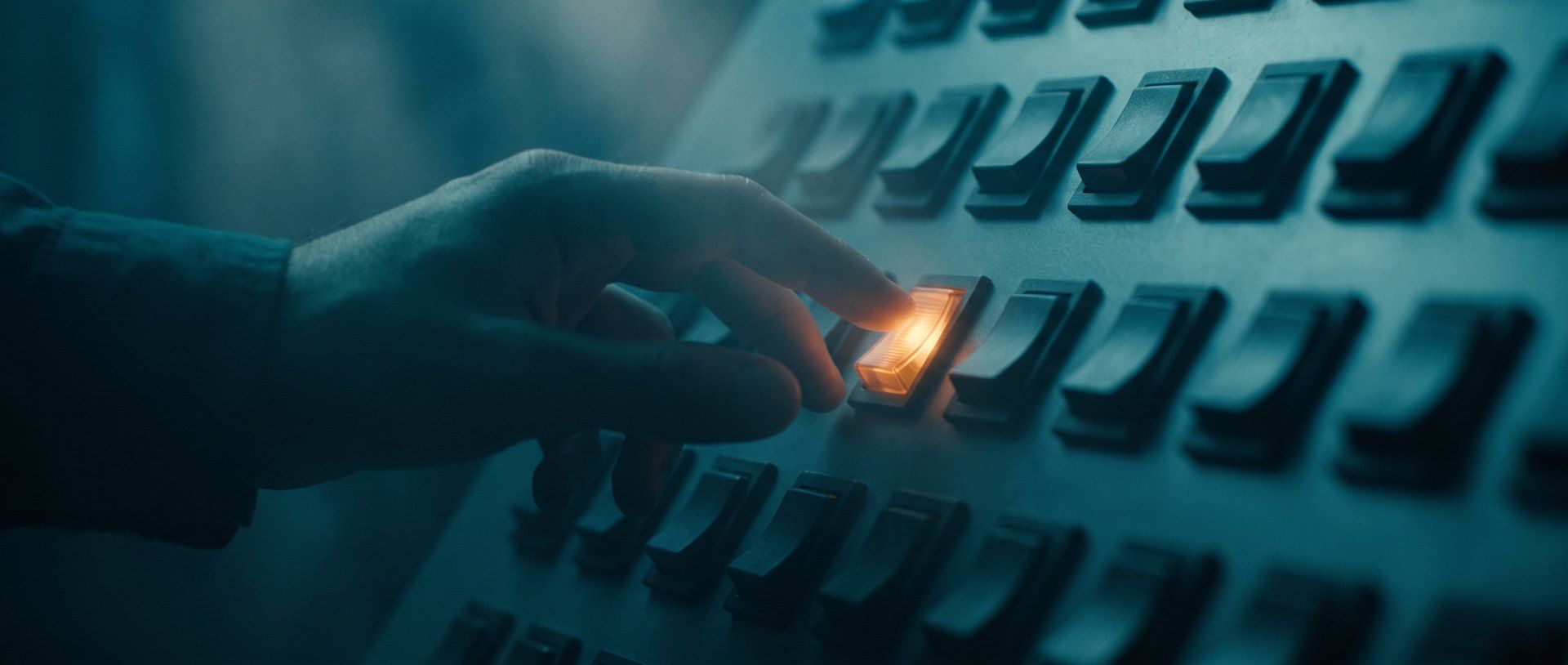 A hand reaching to press one glowing amber switch in a wall of identical dark switches