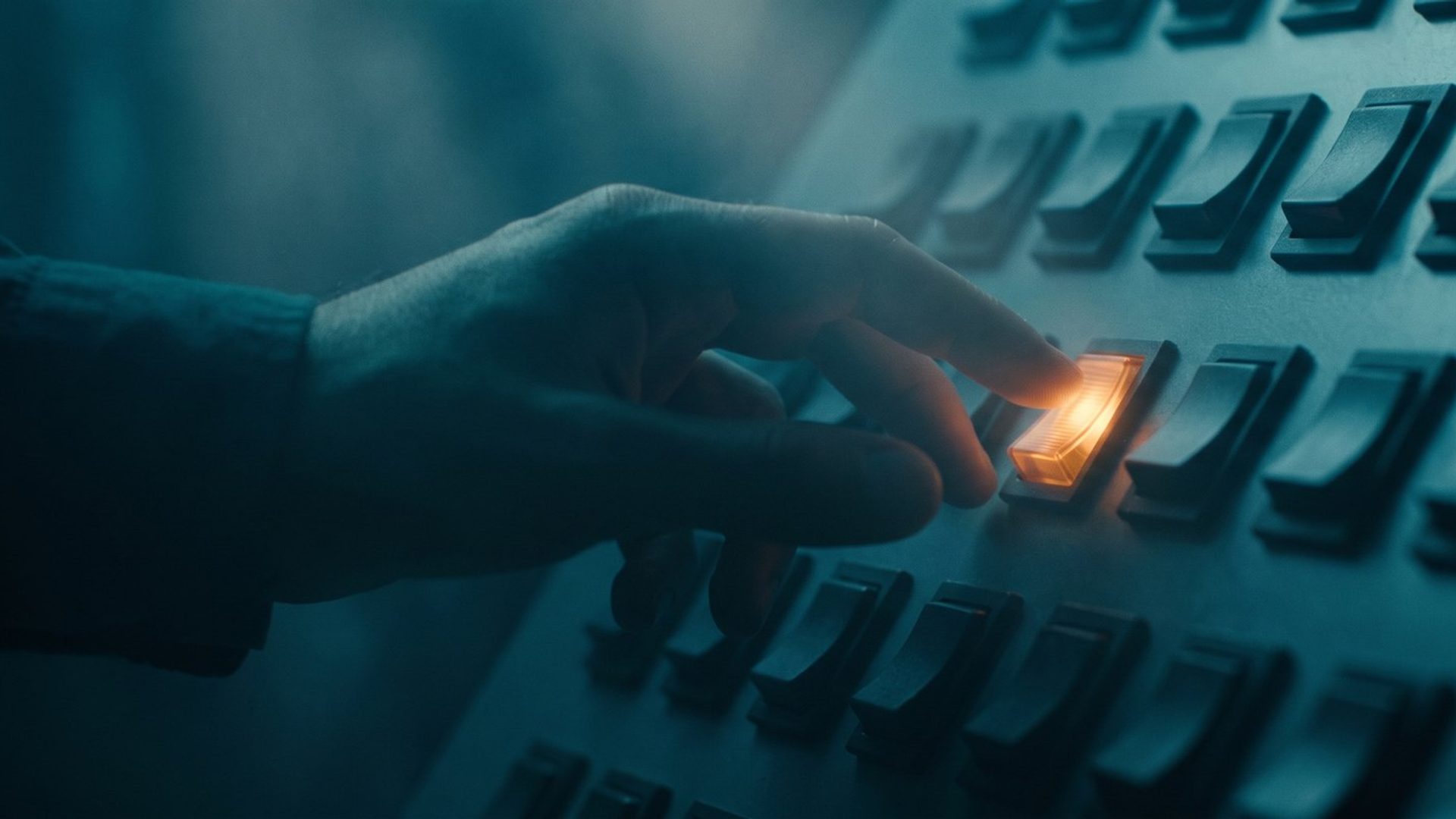 A hand reaching to press one glowing amber switch in a wall of identical dark switches