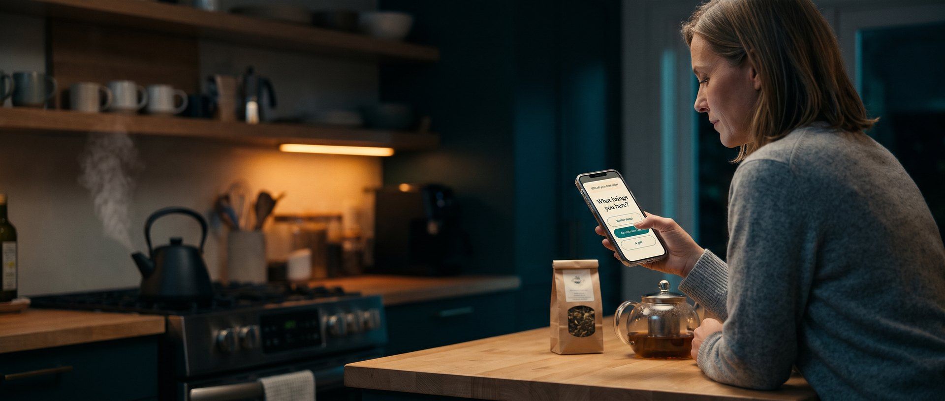 A woman at her kitchen counter in the evening holds her phone, where an online tea shop's signup popup asks What brings you here? with three answer buttons: Better sleep, An afternoon lift, and A gift, while a kettle steams on the stove behind her