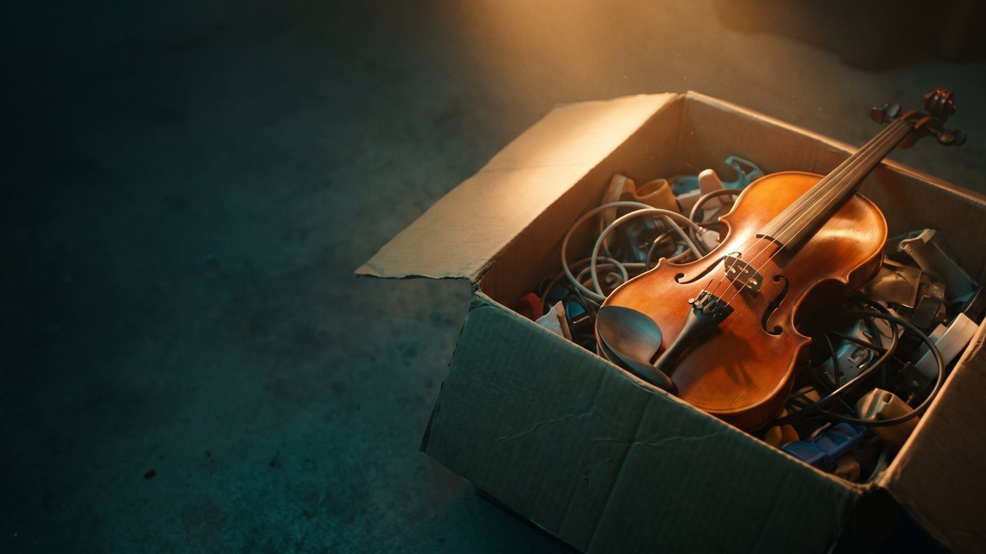 A handcrafted violin with glowing varnished wood lying across an open cardboard box of tangled cables and cheap plastic junk on a dark floor, lit by a single warm amber light.