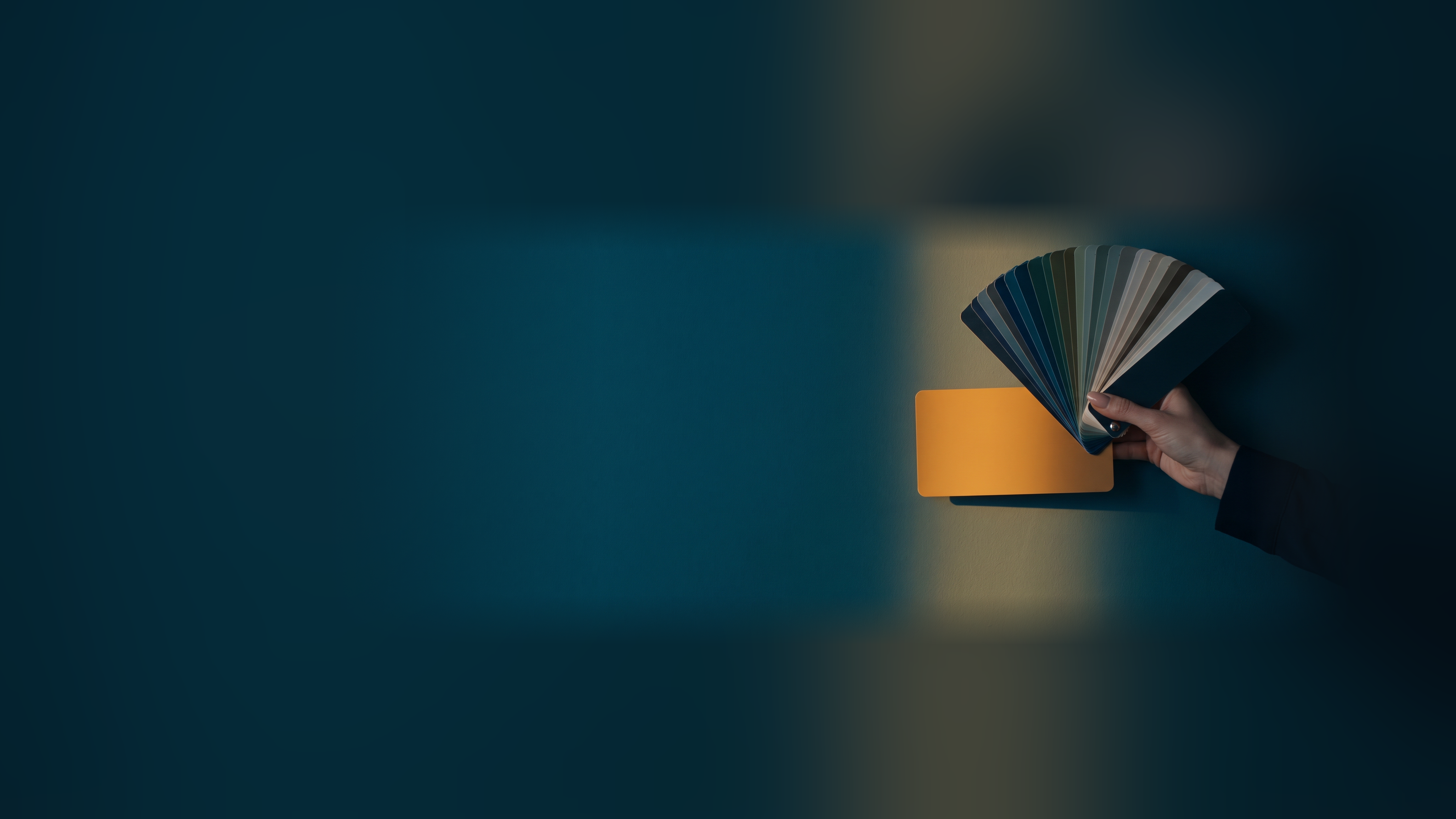 A paint color fan deck held against a wall, one swatch matching the wall exactly