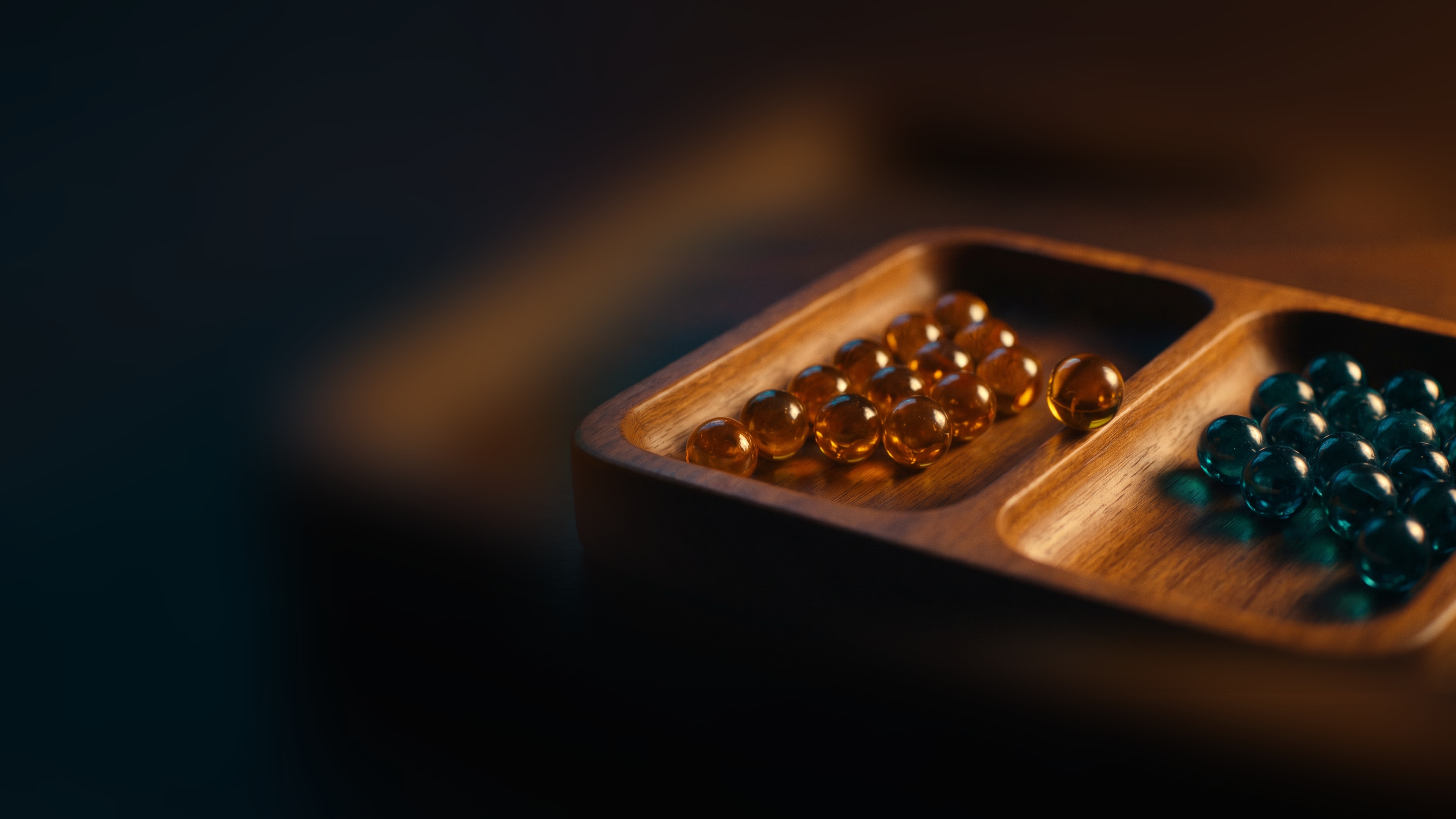 A wooden tray with two compartments, amber marbles gathered in one and teal marbles in the other