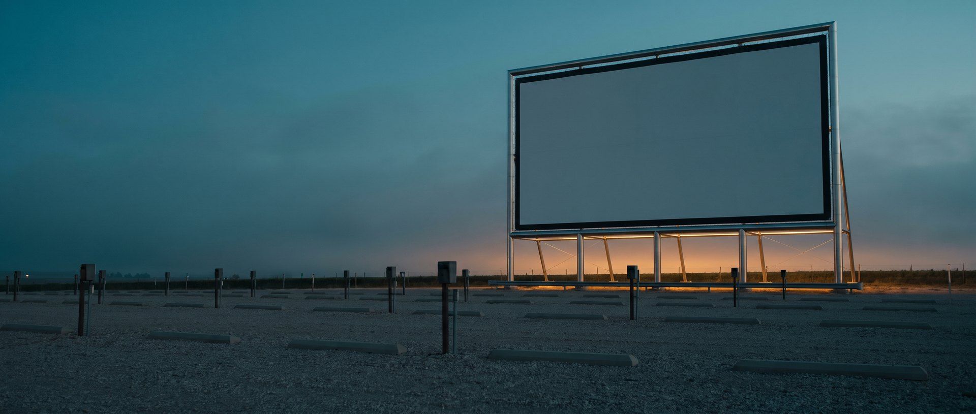 A blank drive-in movie screen standing over an empty lot at dusk