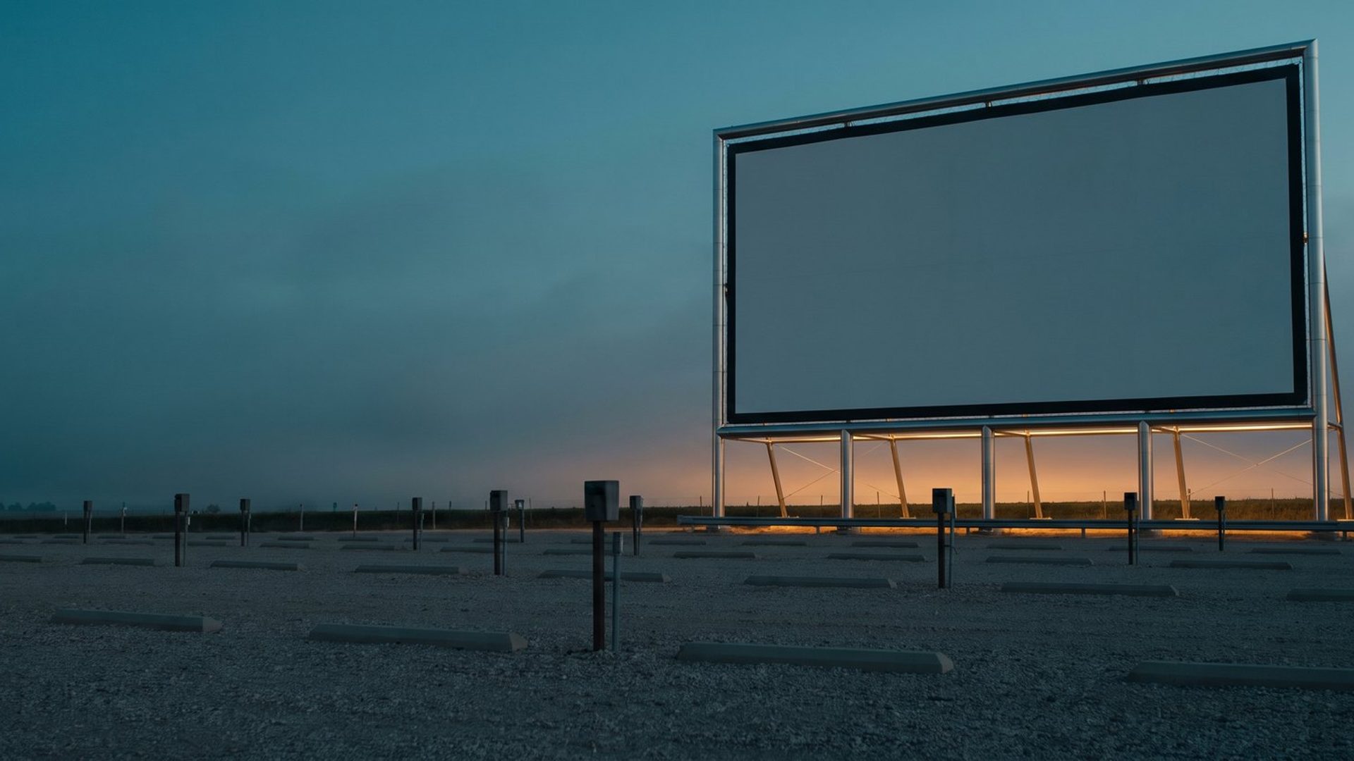 A blank drive-in movie screen standing over an empty lot at dusk