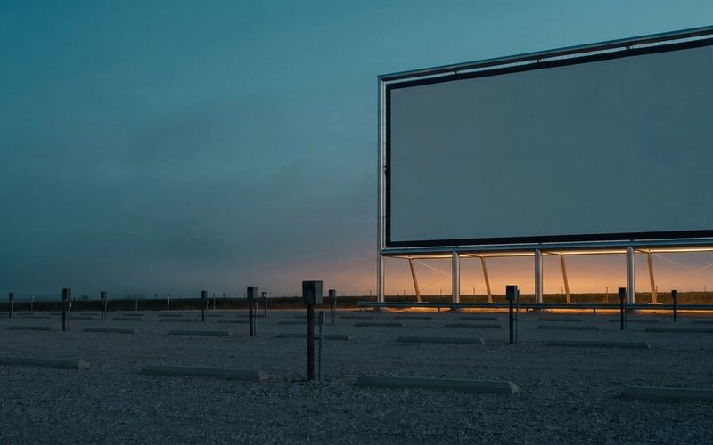 A blank drive-in movie screen standing over an empty lot at dusk