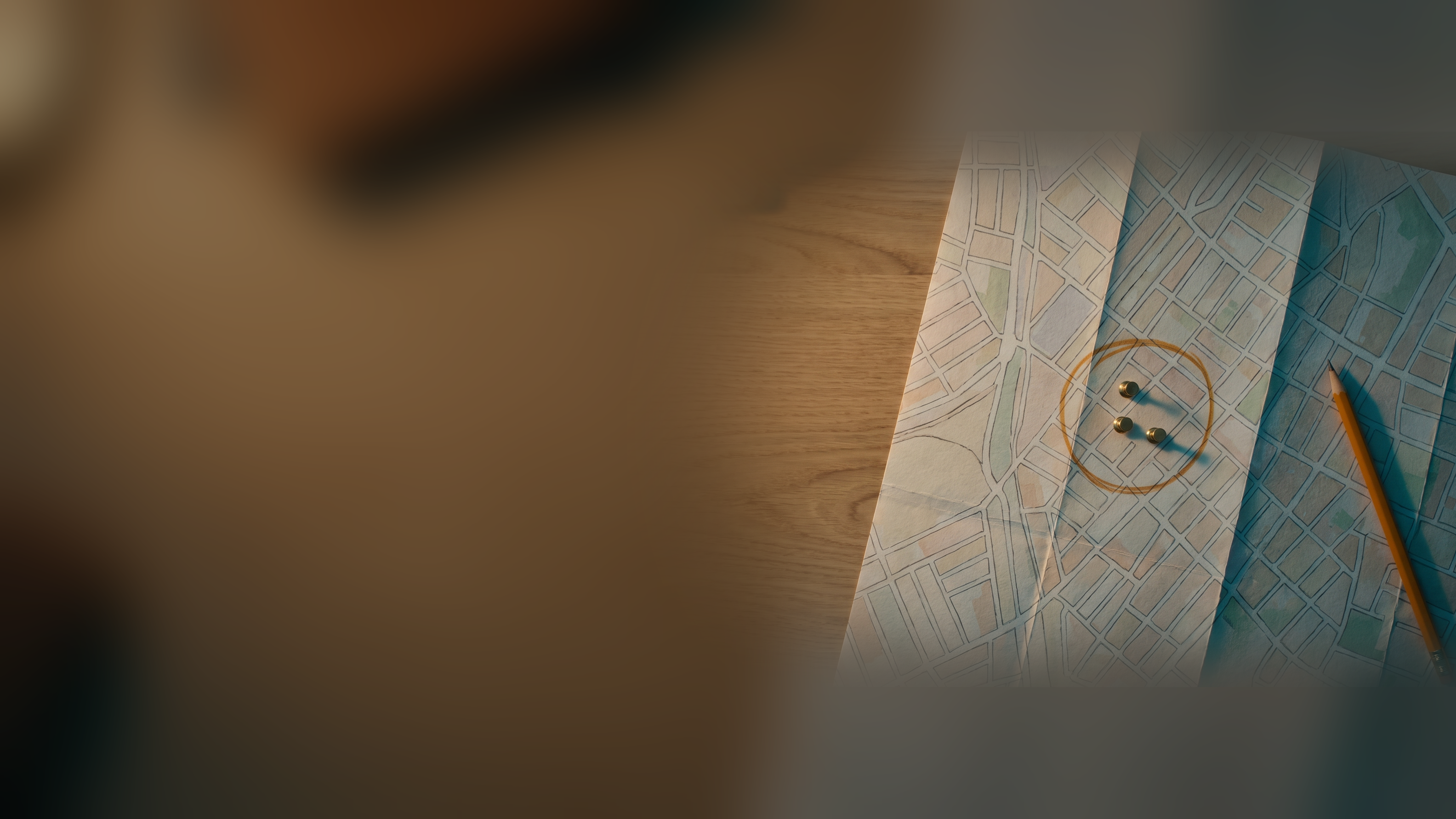 A paper street map on a wooden desk with an amber pencil circle and three pushpins around one neighborhood