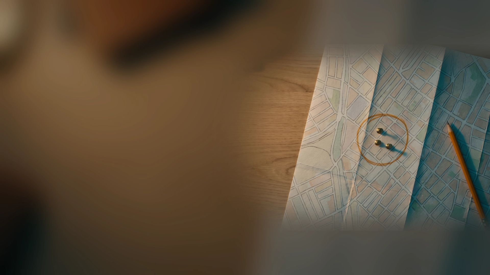 A paper street map on a wooden desk with an amber pencil circle and three pushpins around one neighborhood