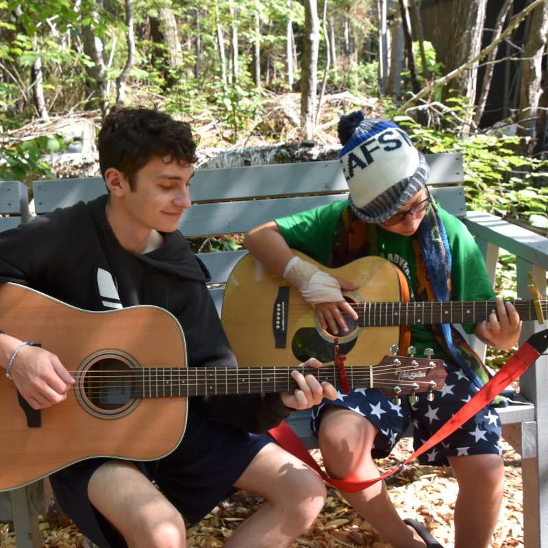 Two campers playing guitar together at camp.
