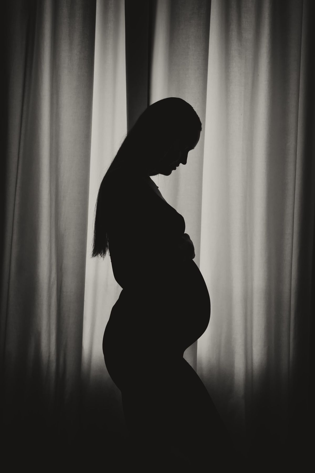 Silhouette d’une future maman à contre-jour devant un rideau