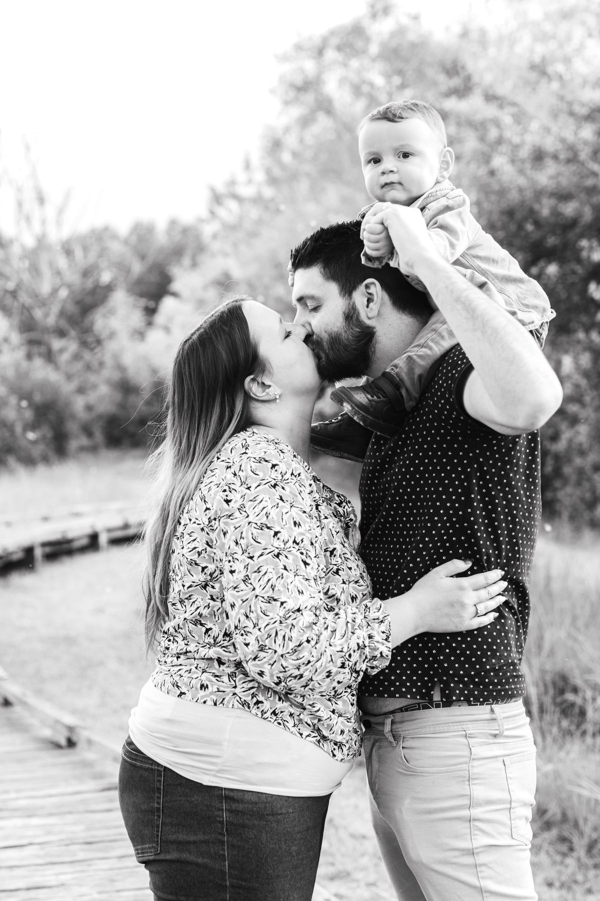 Parents s’embrassant en portant leur bébé à bout de bras, en noir et blanc