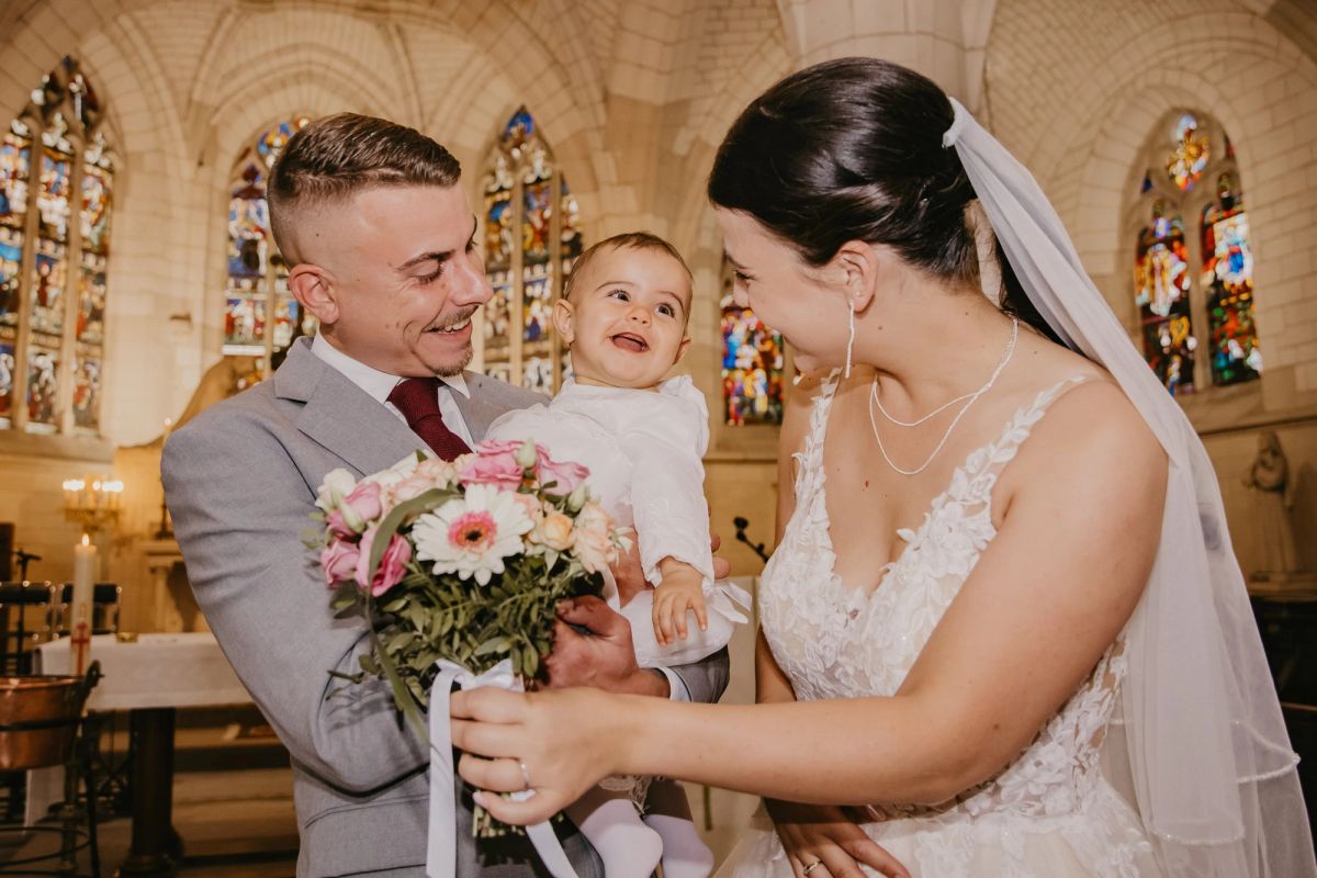 Mariés souriant avec leur bébé dans une église aux vitraux colorés