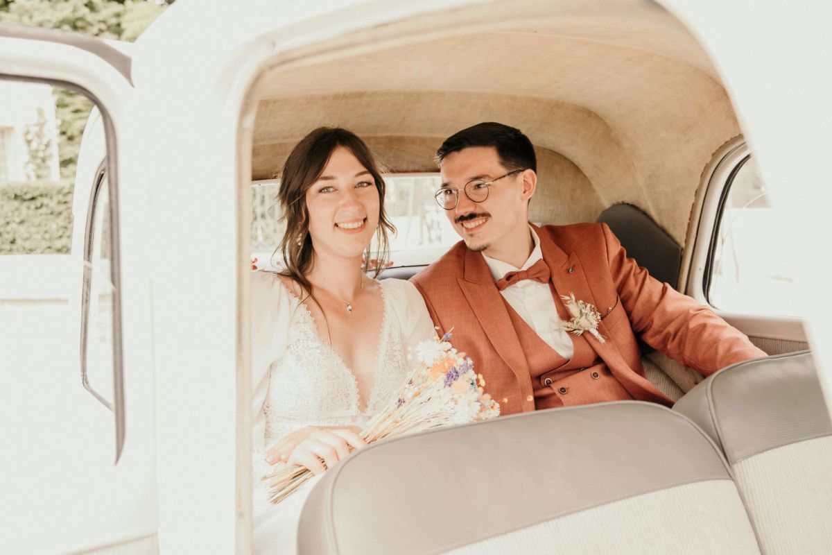 Mariés installés dans une voiture ancienne à la sortie de la cérémonie