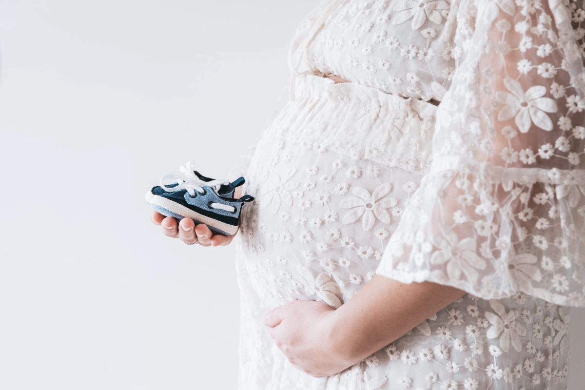 Future maman en robe de dentelle tenant les chaussons de son bébé, séance grossesse dans l’Aube