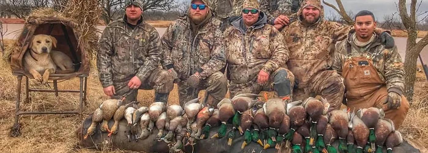 Group of hunters with a dog and a pile of greenhead mallards after a Kansas duck hunt.