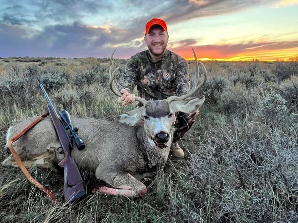 Hunter with a trophy mule deer buck overlooking rugged Western terrain