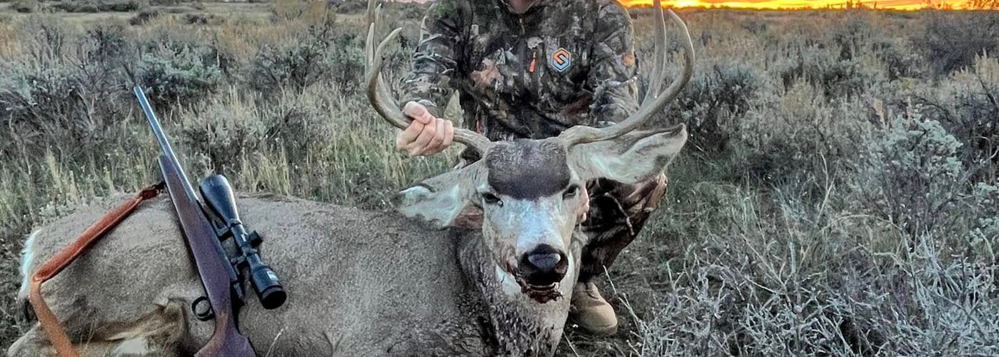 Hunter with a trophy mule deer buck overlooking rugged Western terrain