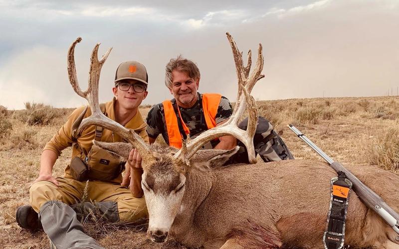 Hunter with a trophy mule deer buck in Colorado mountain terrain