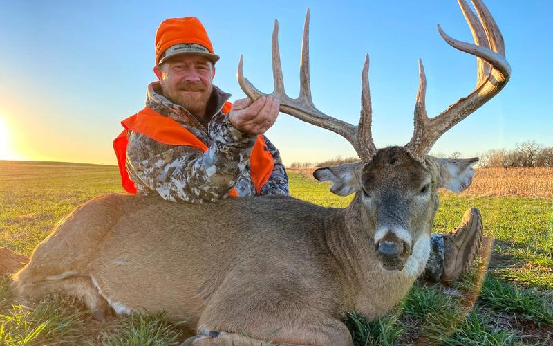 Hunter with large Kansas whitetail buck posed in agricultural fields during hunting season