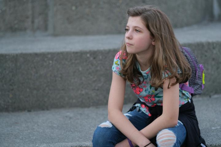 Ragazza seduta sui gradini con lo zaino, sguardo lontano