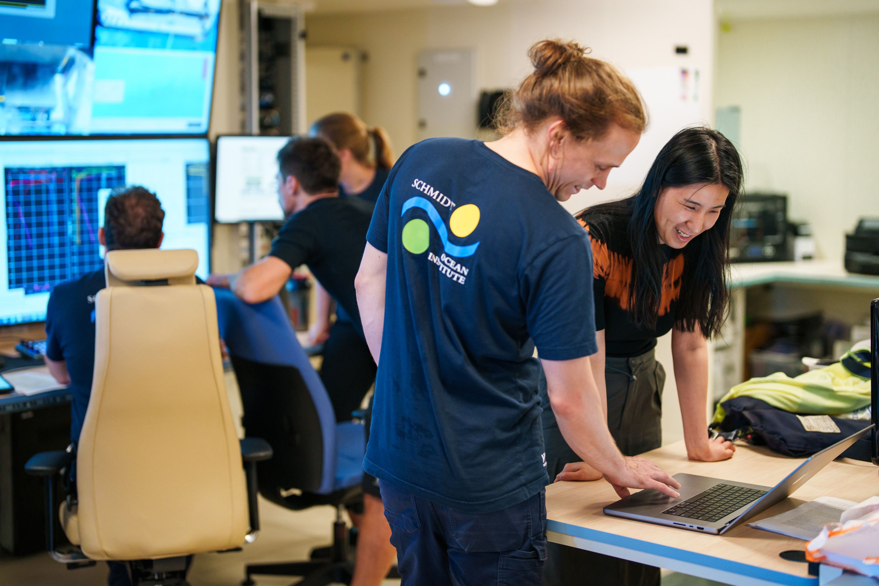 people working together in a control room looking at screens of data