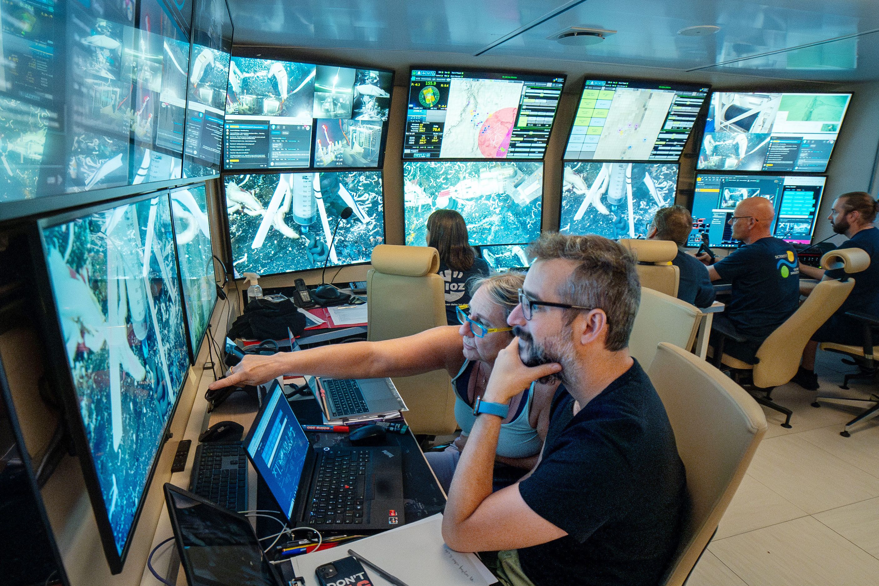 people in control room looking at full wall of screens