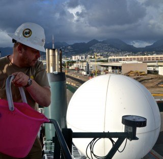 Marine technician Paul "Jimbo" Duncan washing a sunlight (Photosynthetically Active Radiation) sensor mounted on Falkor's main mast.