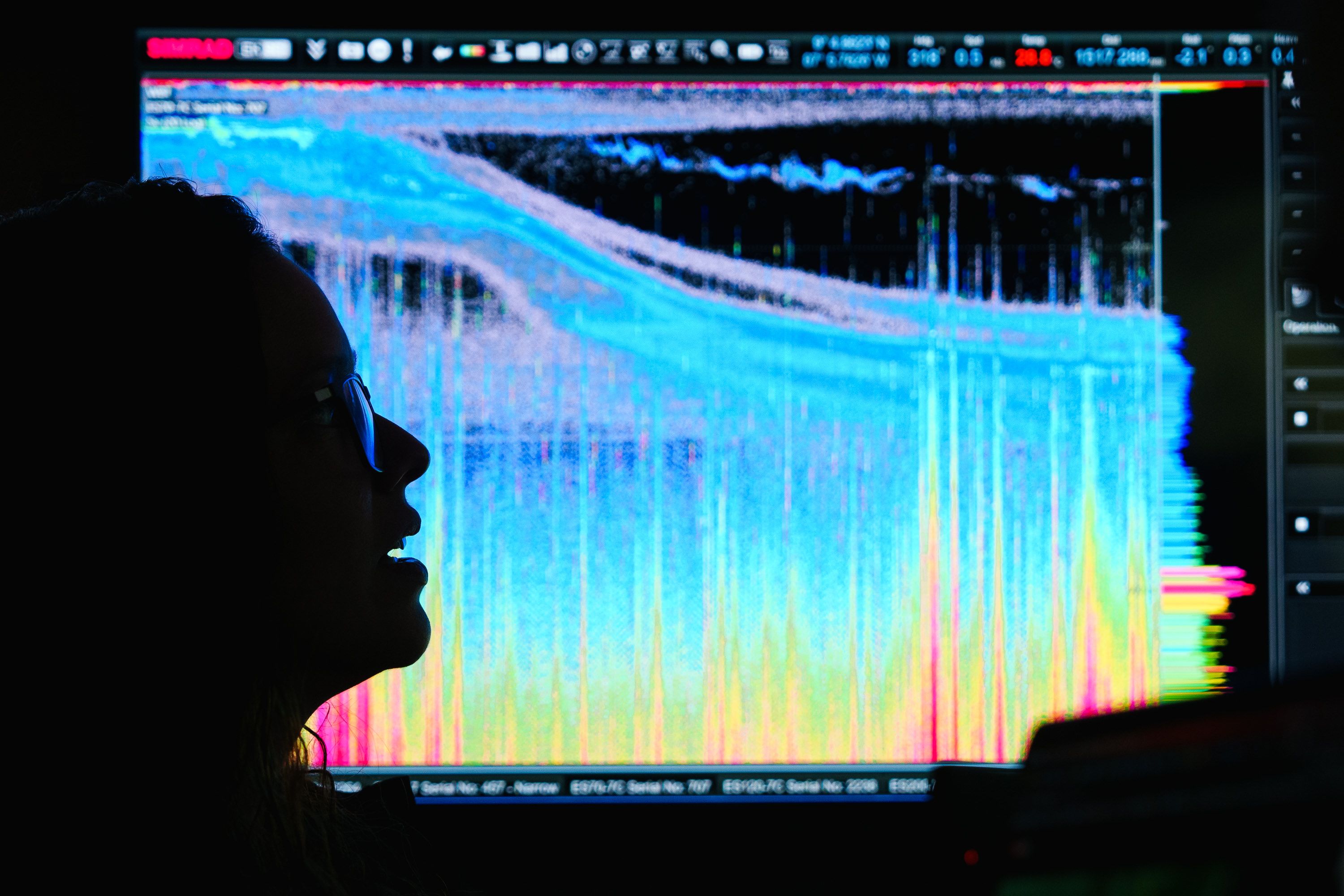 A person with glasses is silhouetted against a large ocean data set. 