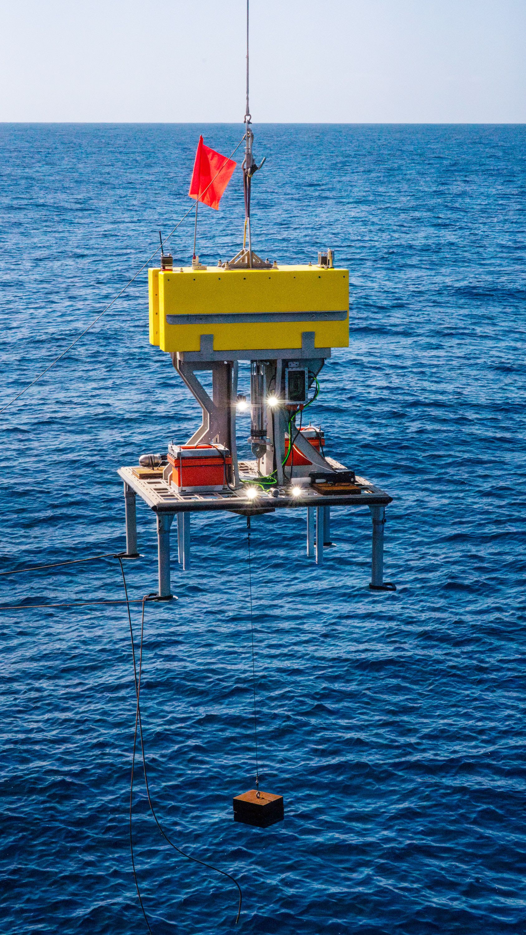 Lander with a rectangular yellow floatation block, equipped with cameras lights and batteries as it gets deployed during sea trials. 