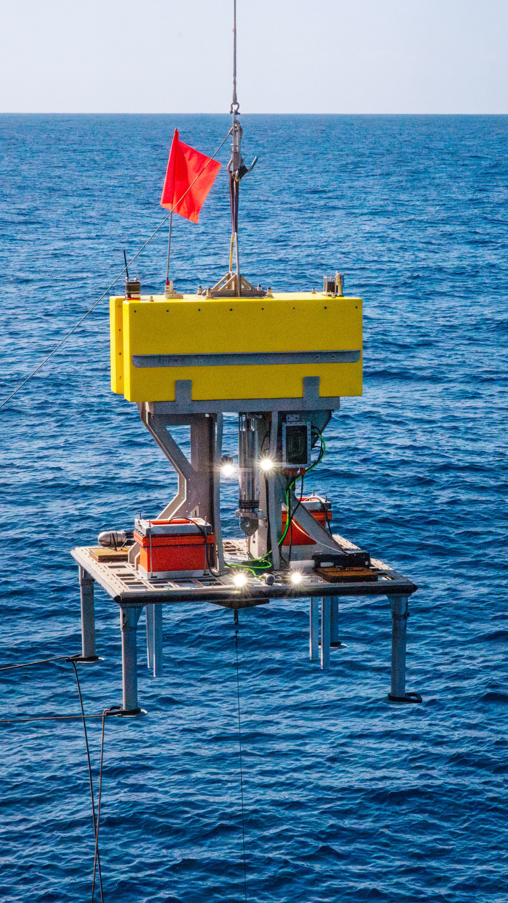 Lander with a rectangular yellow floatation block, equipped with cameras lights and batteries as it gets deployed during sea trials.