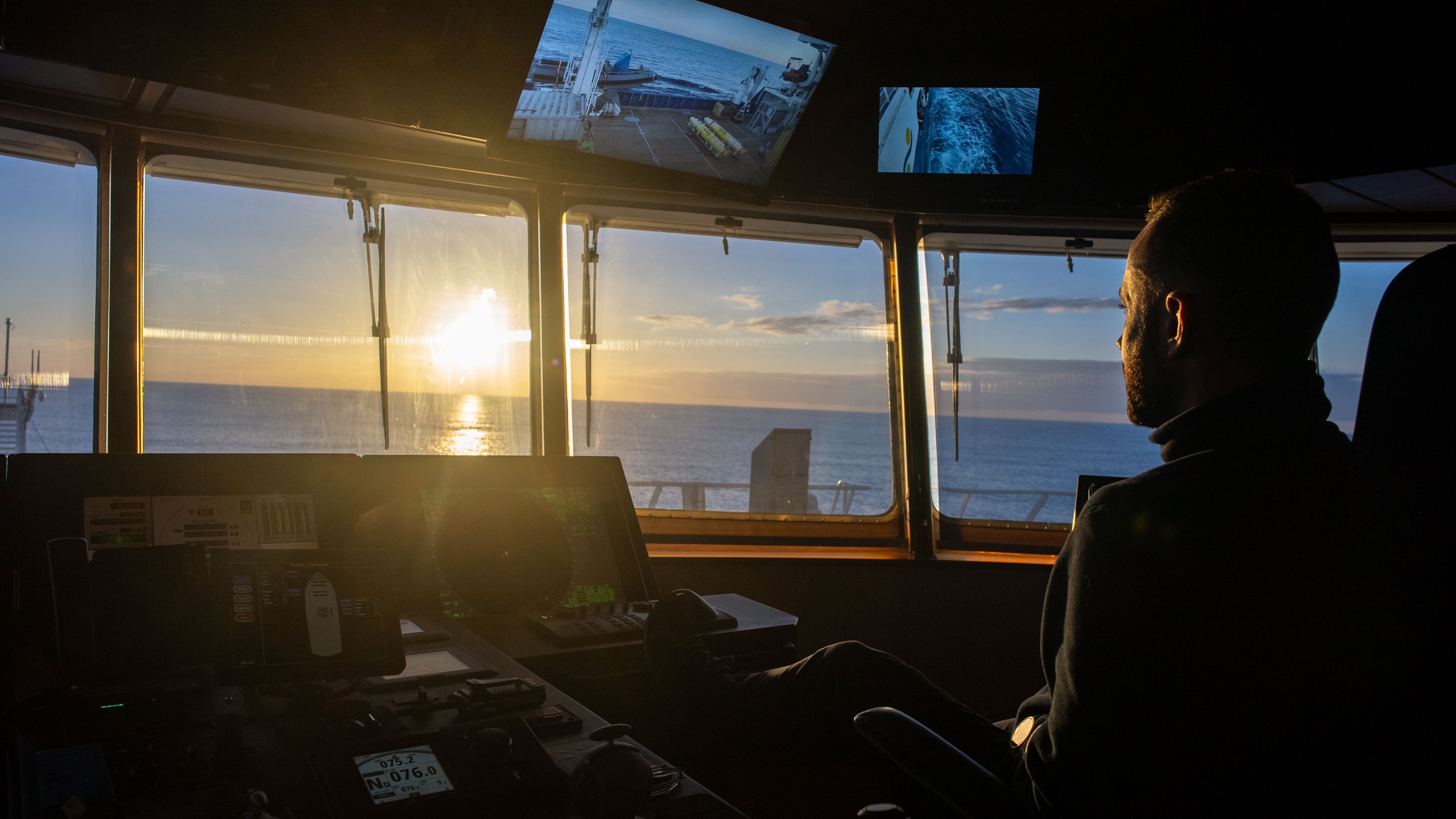 Bridge officer looking into the sunset while driving the ship.