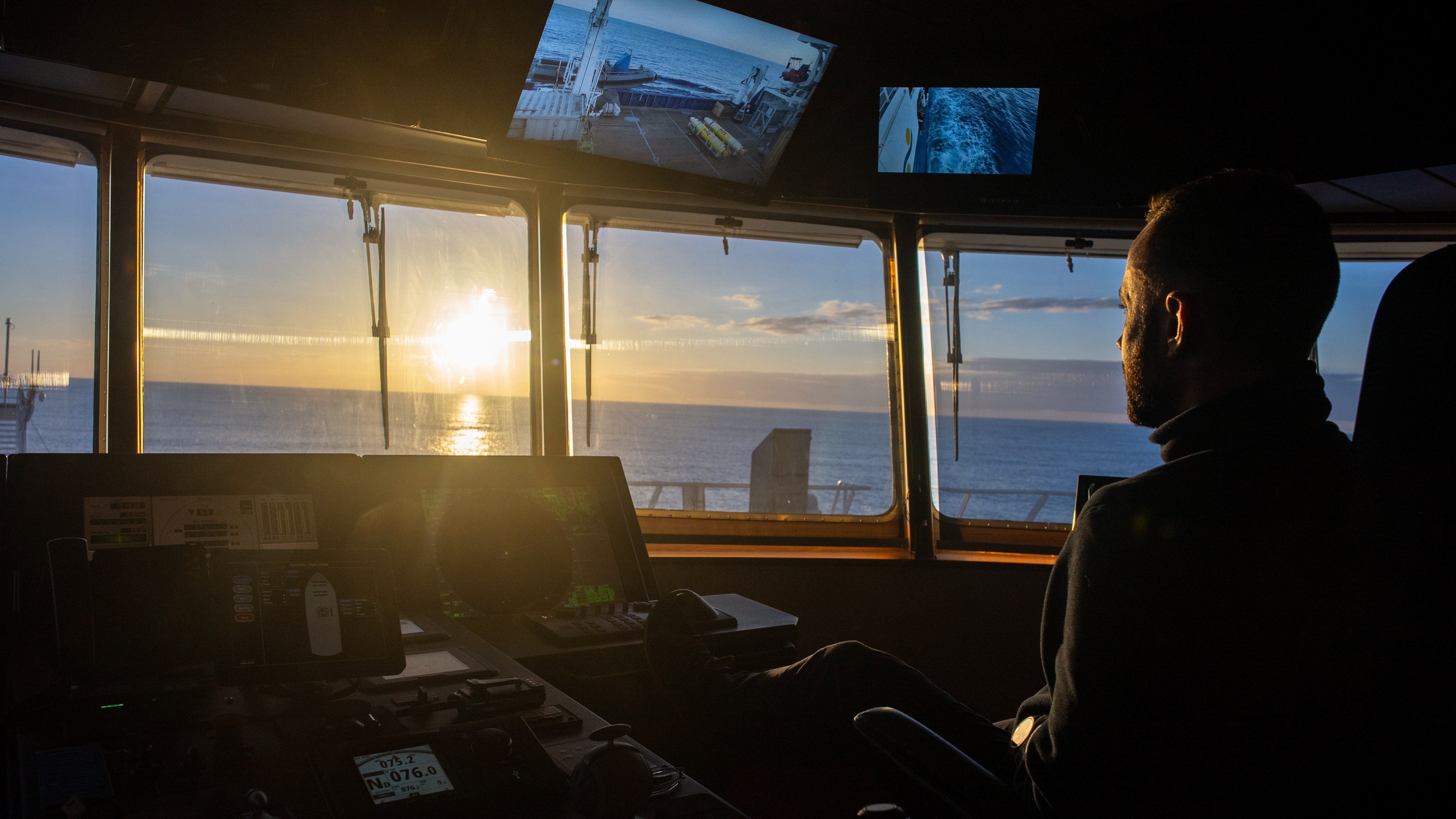 Bridge officer looking into the sunset while driving the ship.