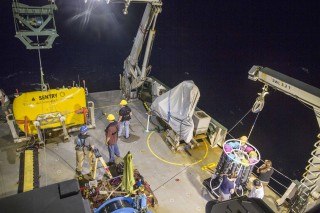The autonomous underwater vehicle Sentry (yellow, at left) is prepared for deployment off the stern of the R/V Falkor, after a trace-metal CTD instrument package and water sampler is recovered (lower right).