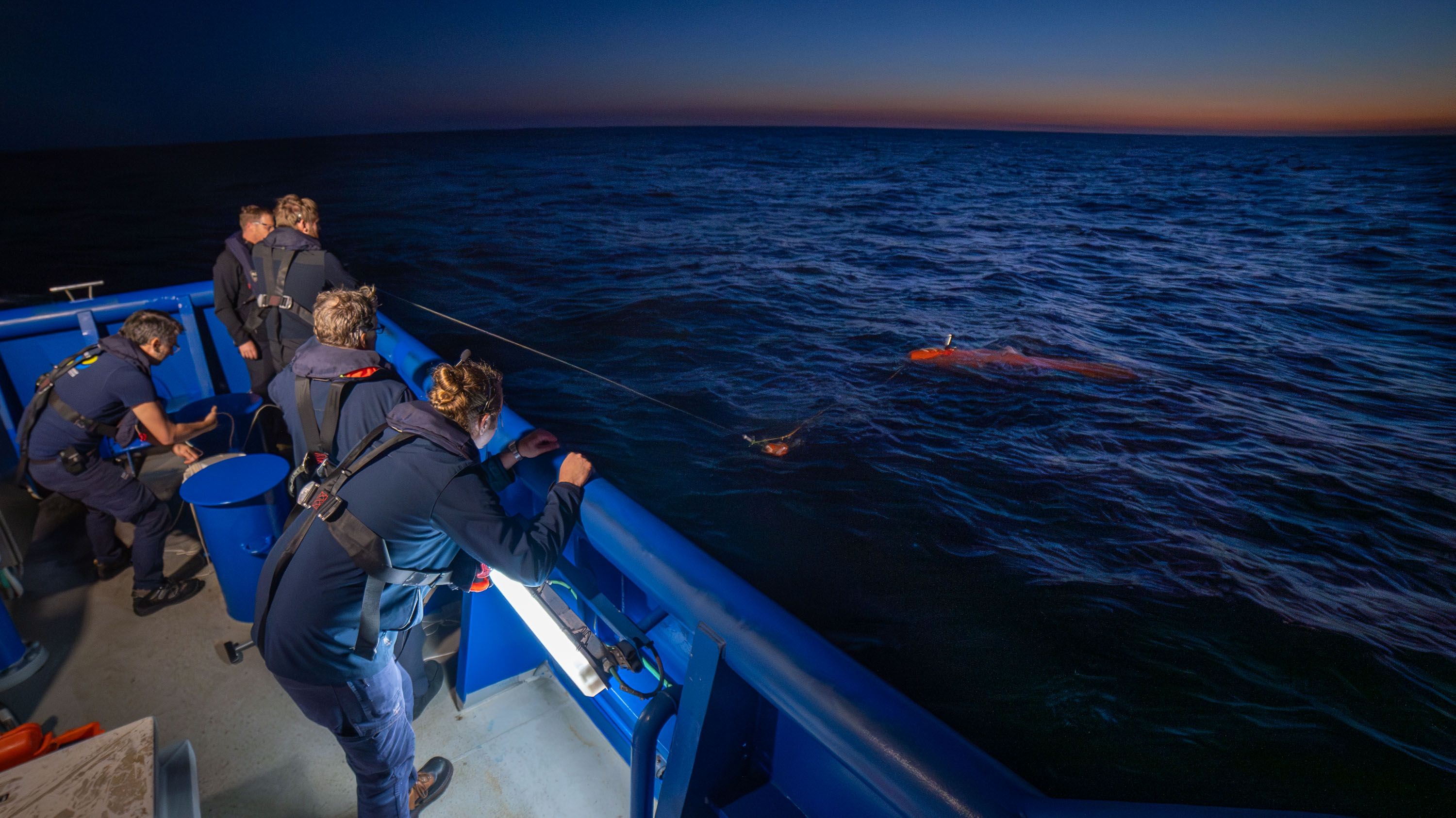 AUV technicians gather on the back deck as they commence recovery of the AUV after sunset. 