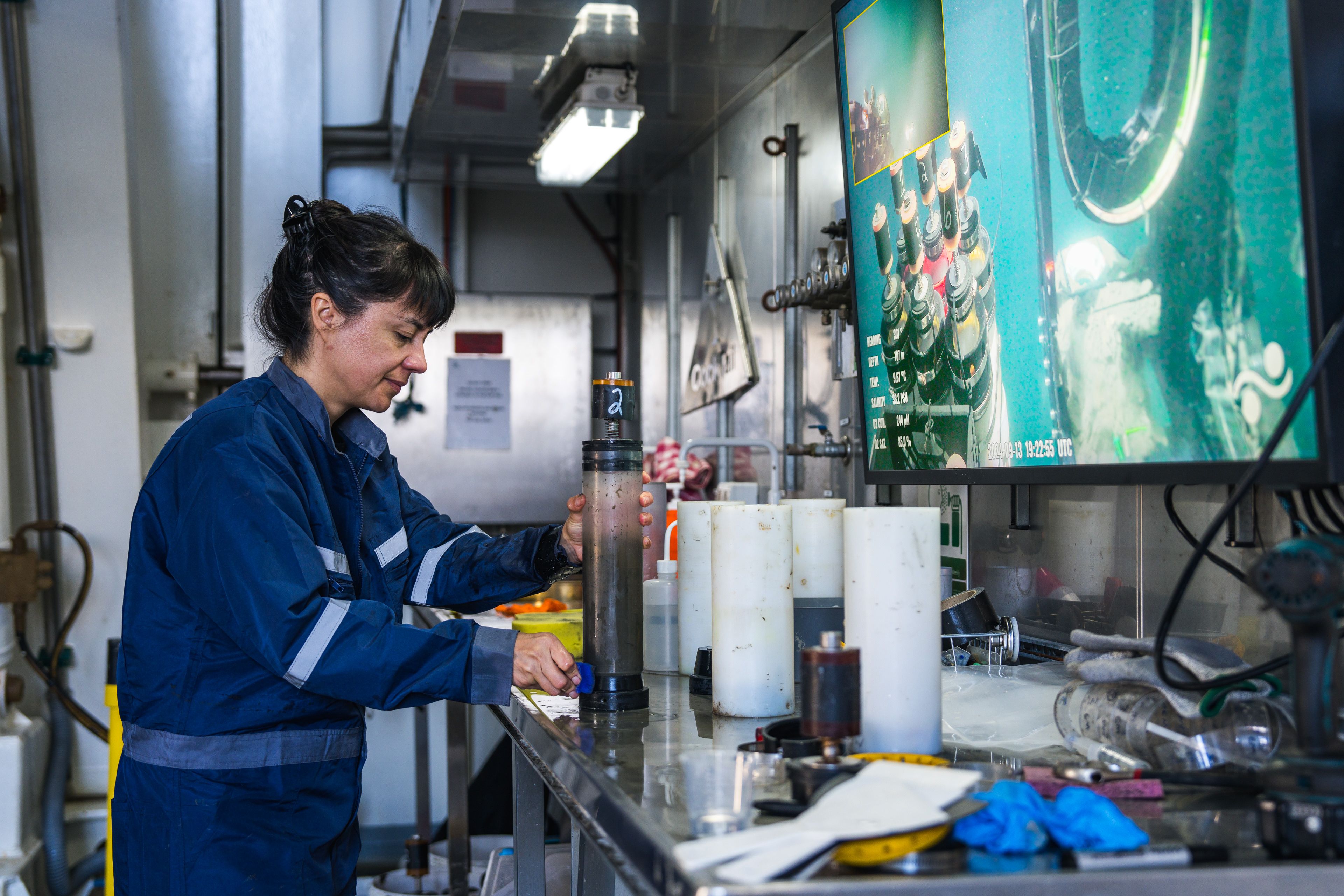 Person working in lab with cylinders and screens with ocean in background