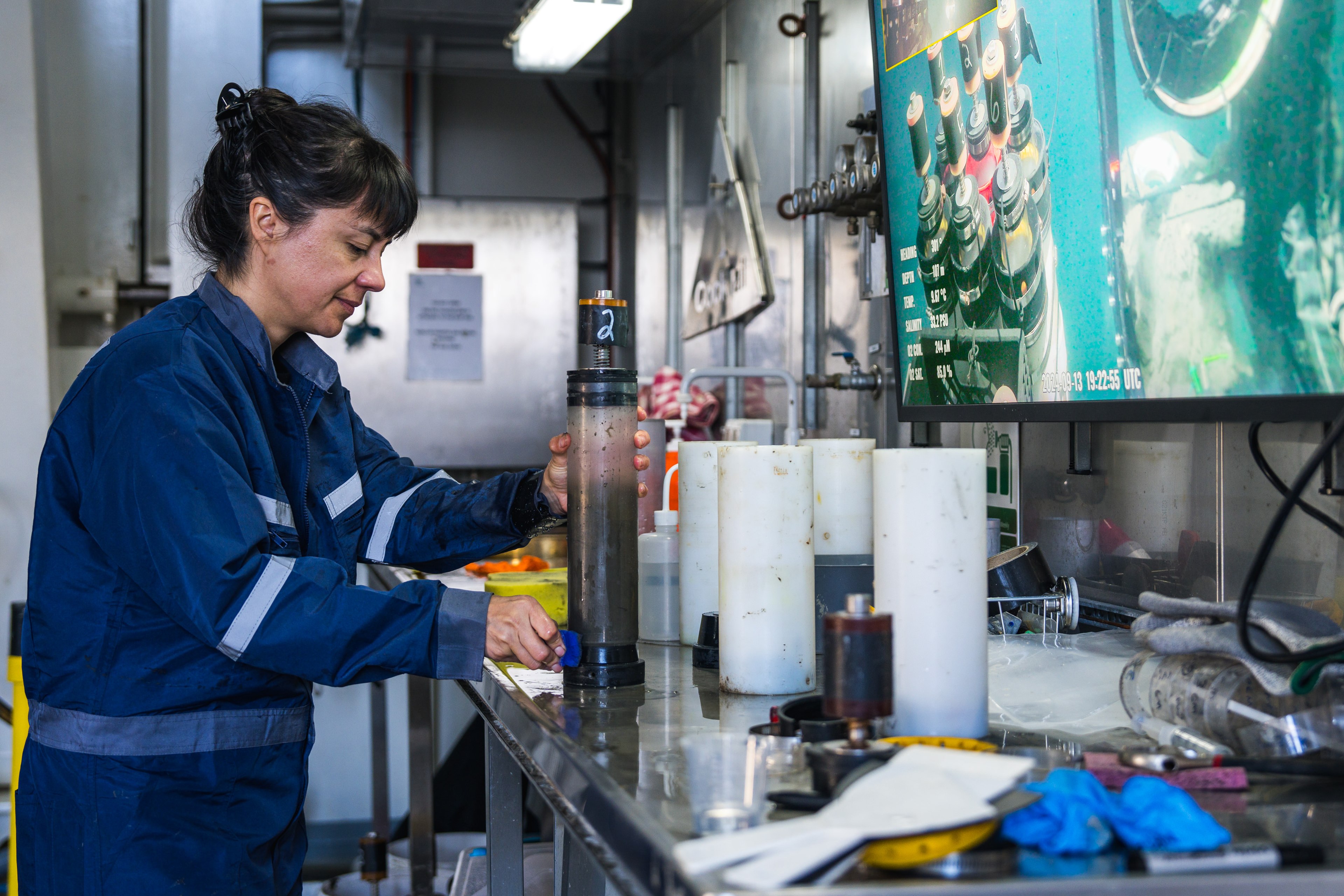 Person working in lab with cylinders and screens with ocean in background