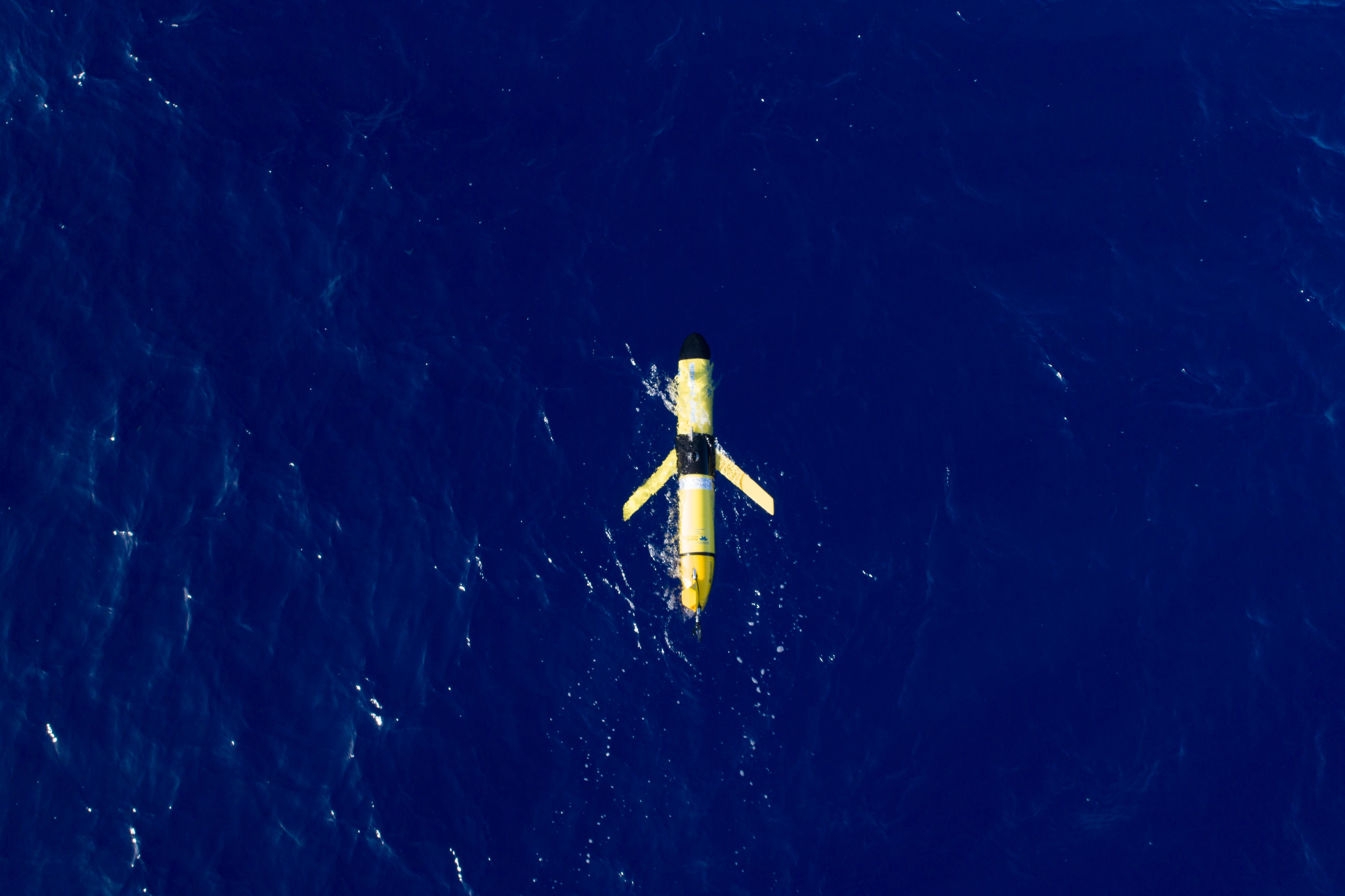 A yellow glider sits at the surface of a bright, blue ocean. 