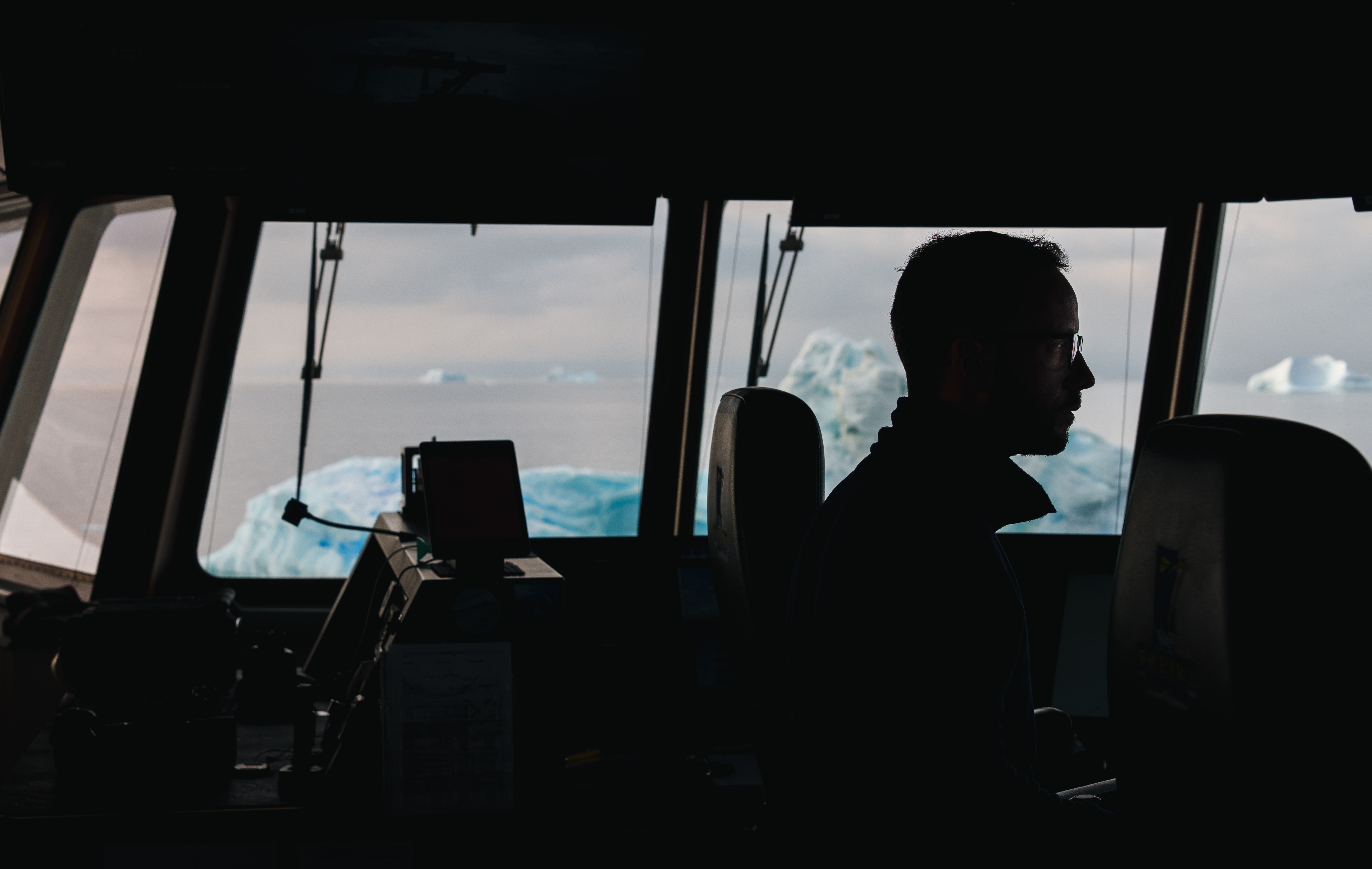 Silhouette of a man at a window, an iceberg floats on ocean behind.