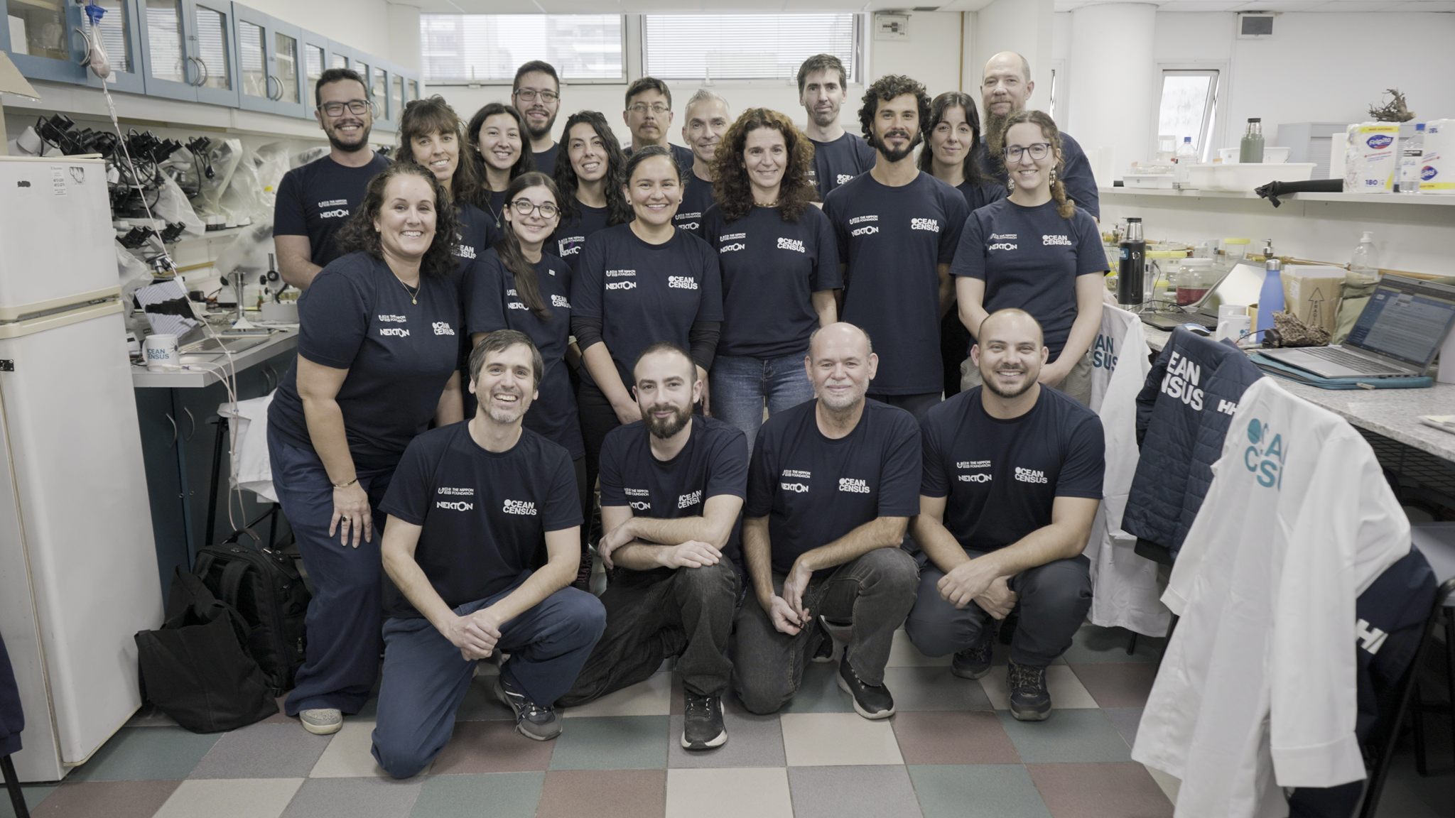 Group portrait of the Argentina Species Discovery Workshop team posing together inside a science laboratory wearing matching Ocean Census t-shirts.