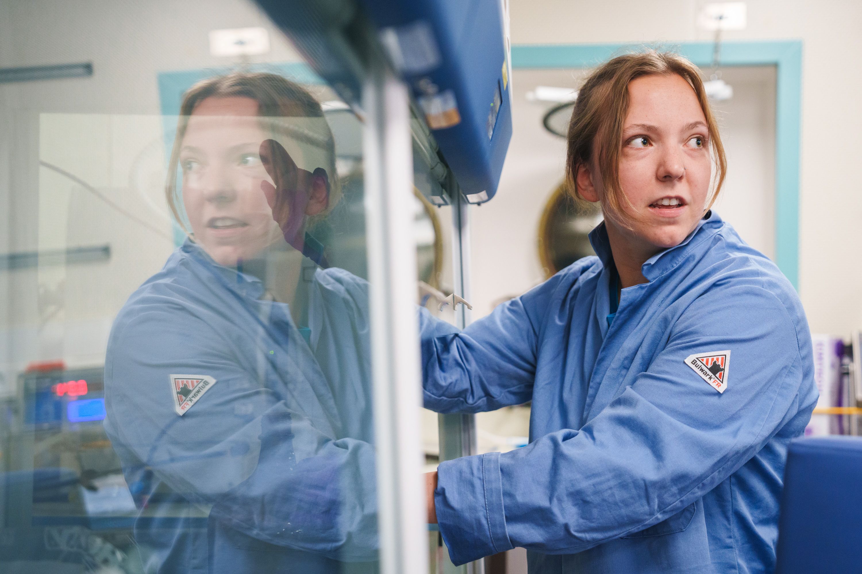 Scientist wearing a blue lab coat working with chemicals inside the fume hood in the labs. 