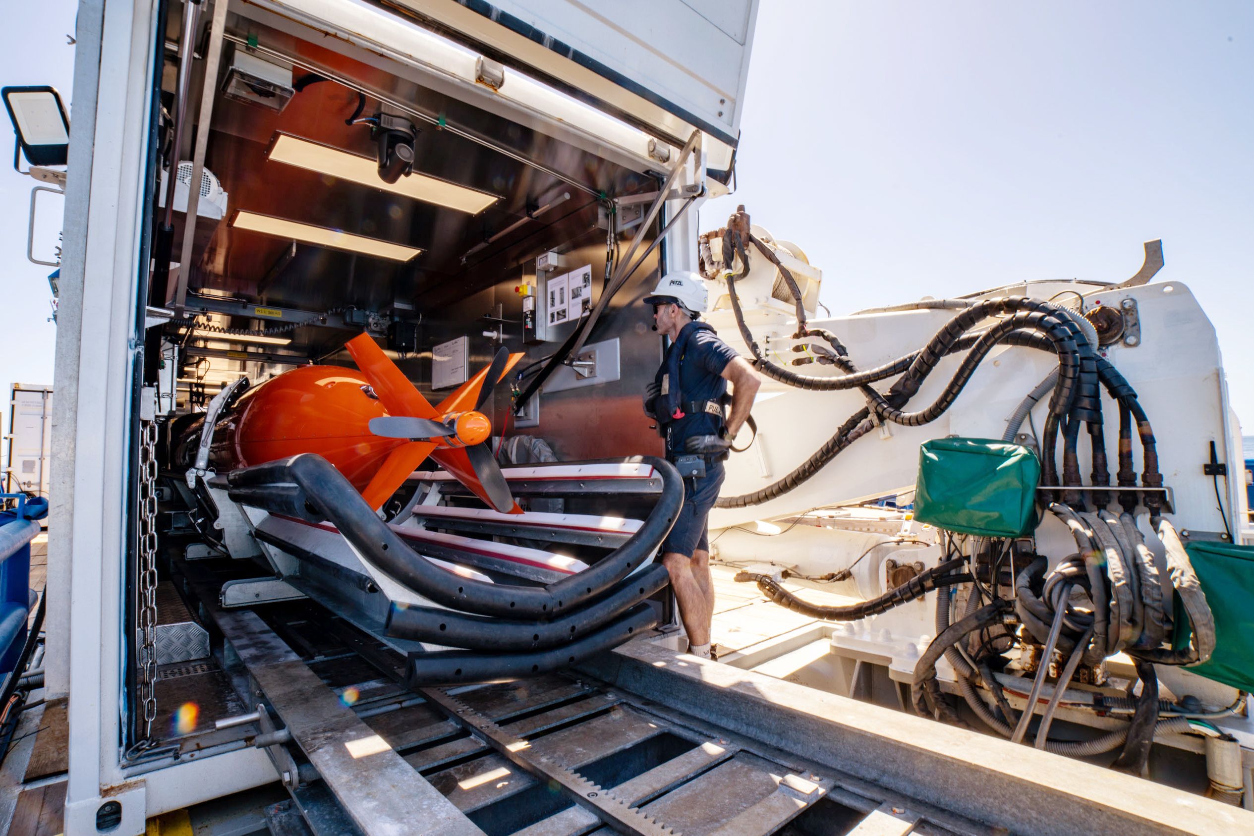 AUV technician monitors the AUV as it is being moved from the storage van to deployment position. The rudder and propellers are visible. 