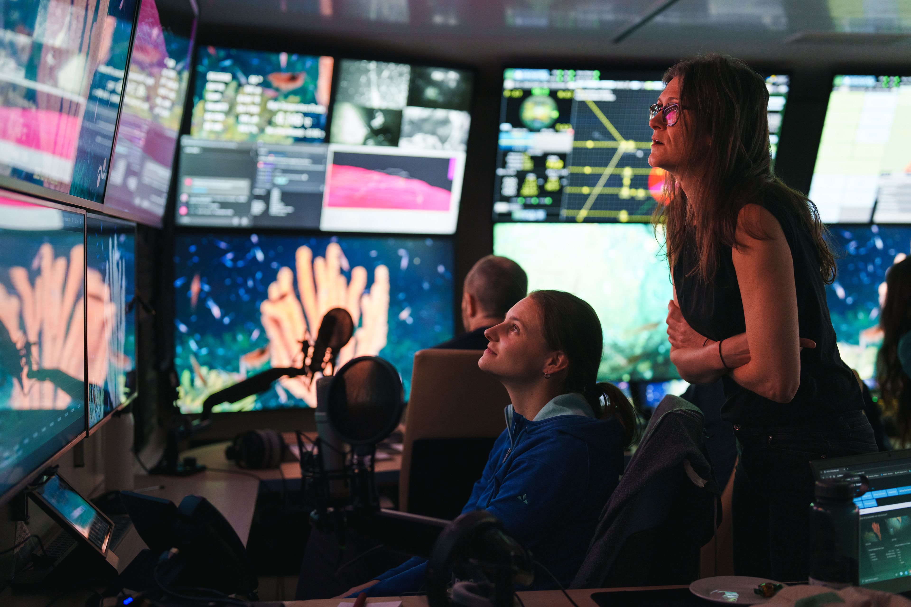 Two scientists in the mission control room looking at screens showing a large sponge.