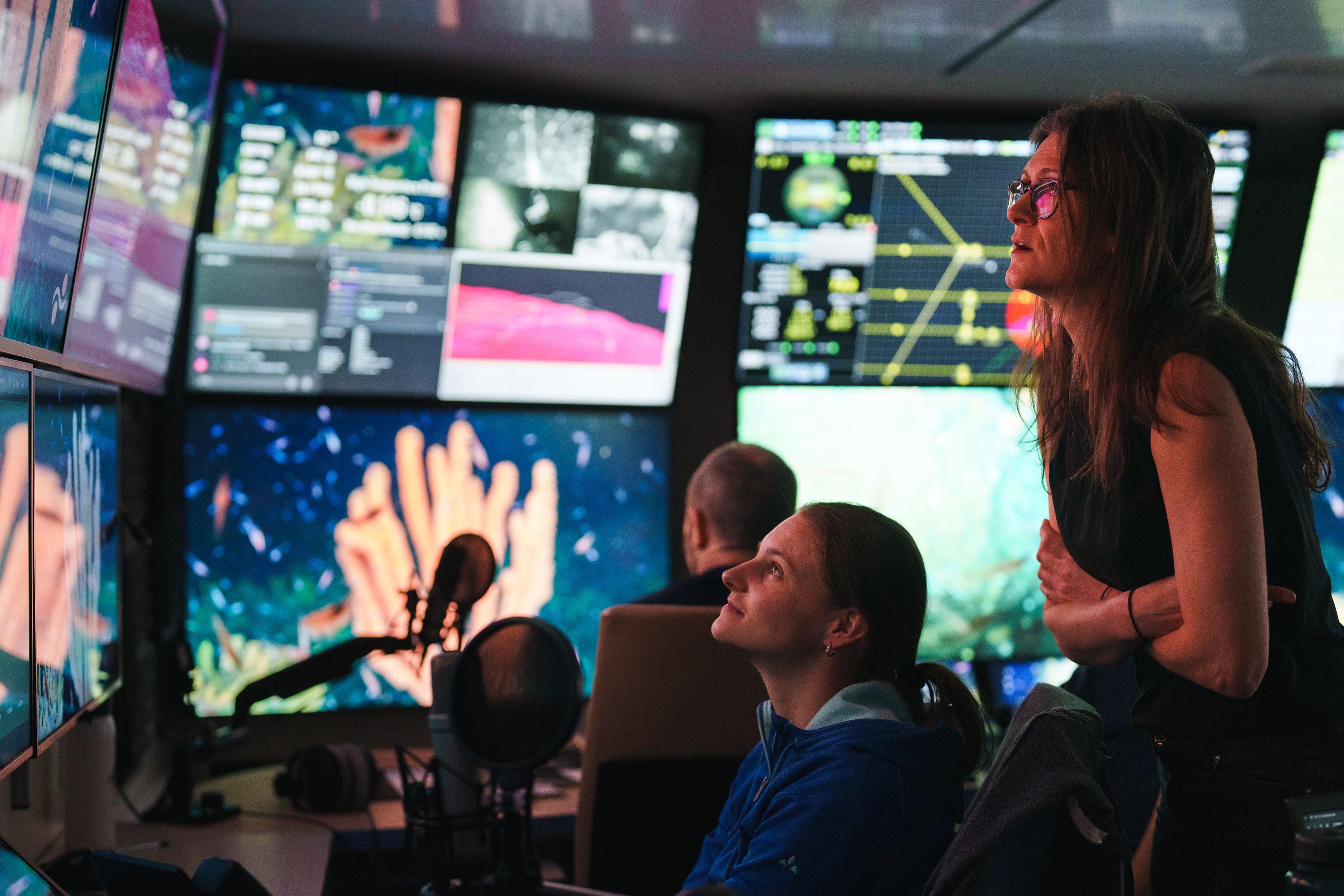 Two scientists in the mission control room looking at screens showing a large sponge.