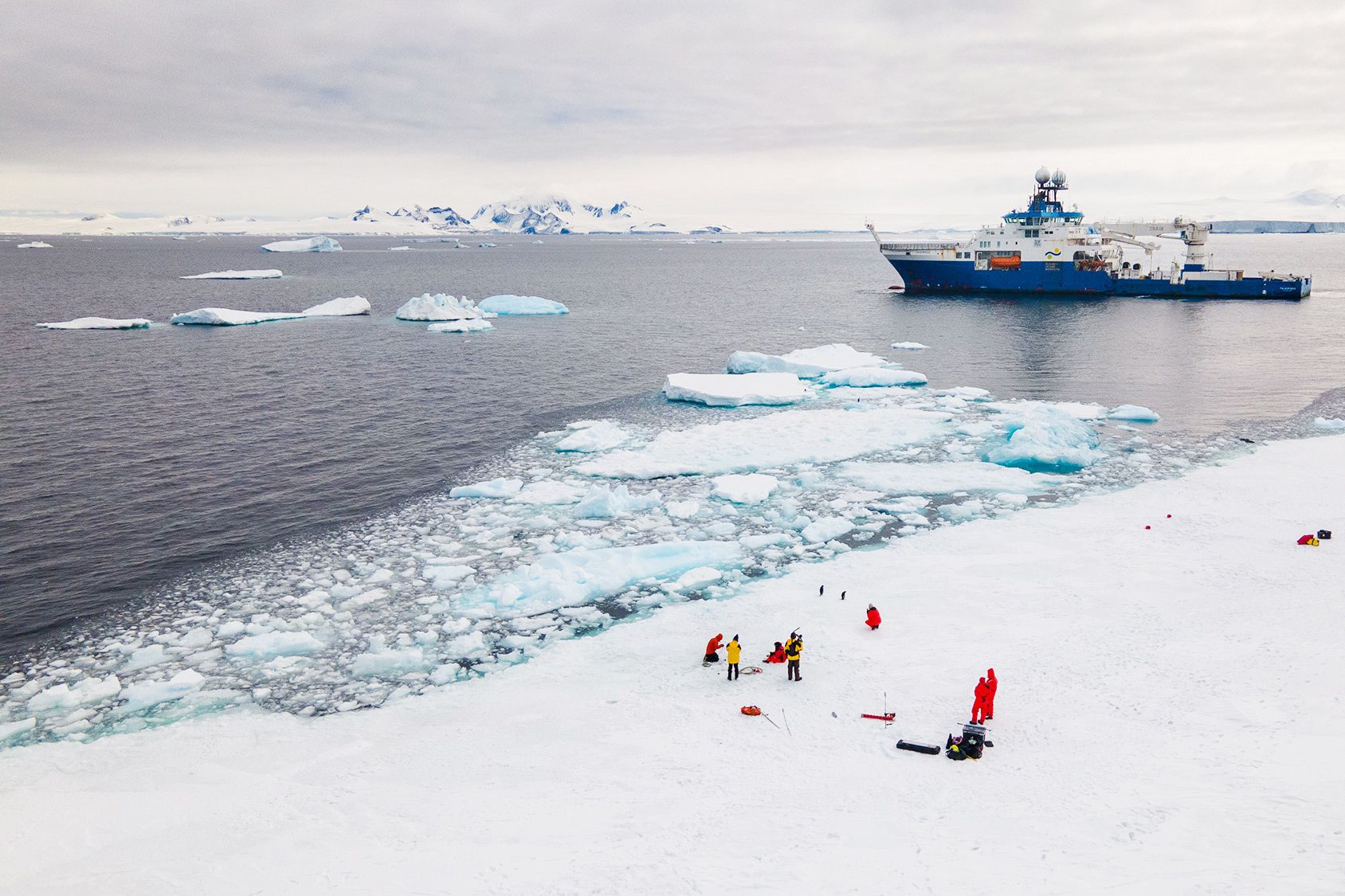  Researchers on the ice in Antarctica with research vessel in background