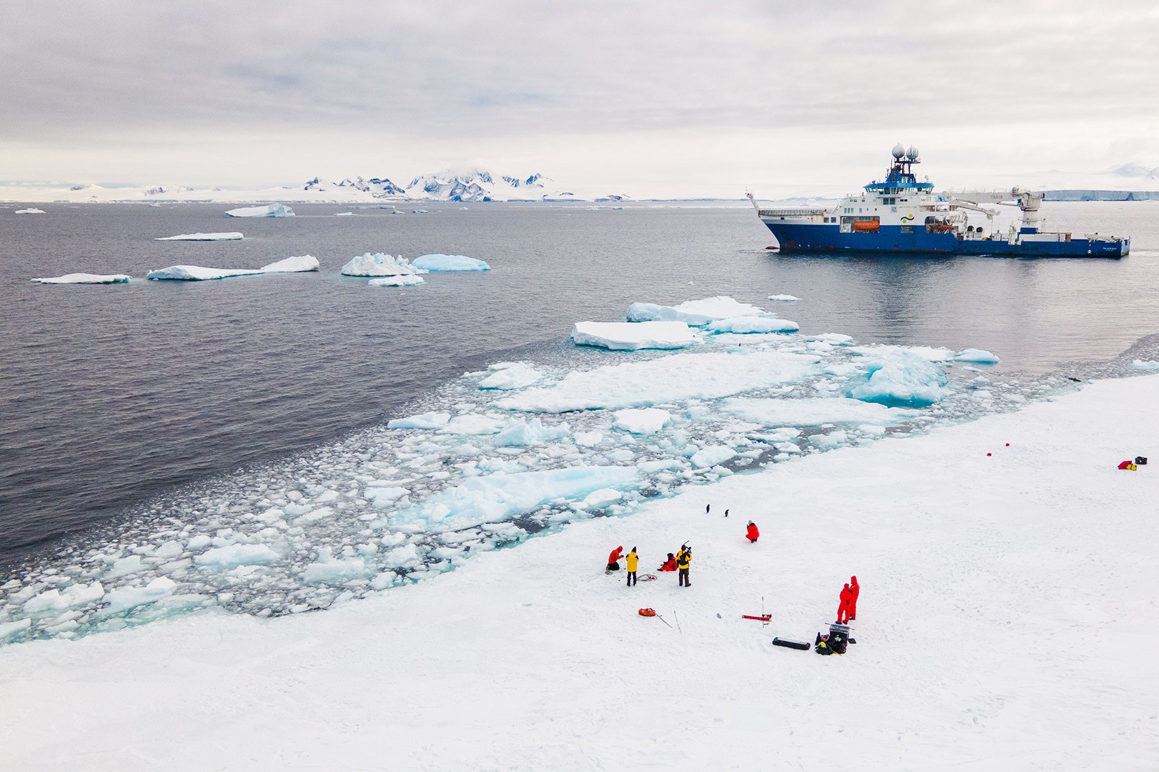 Researchers on the ice in Antarctica with research vessel in background