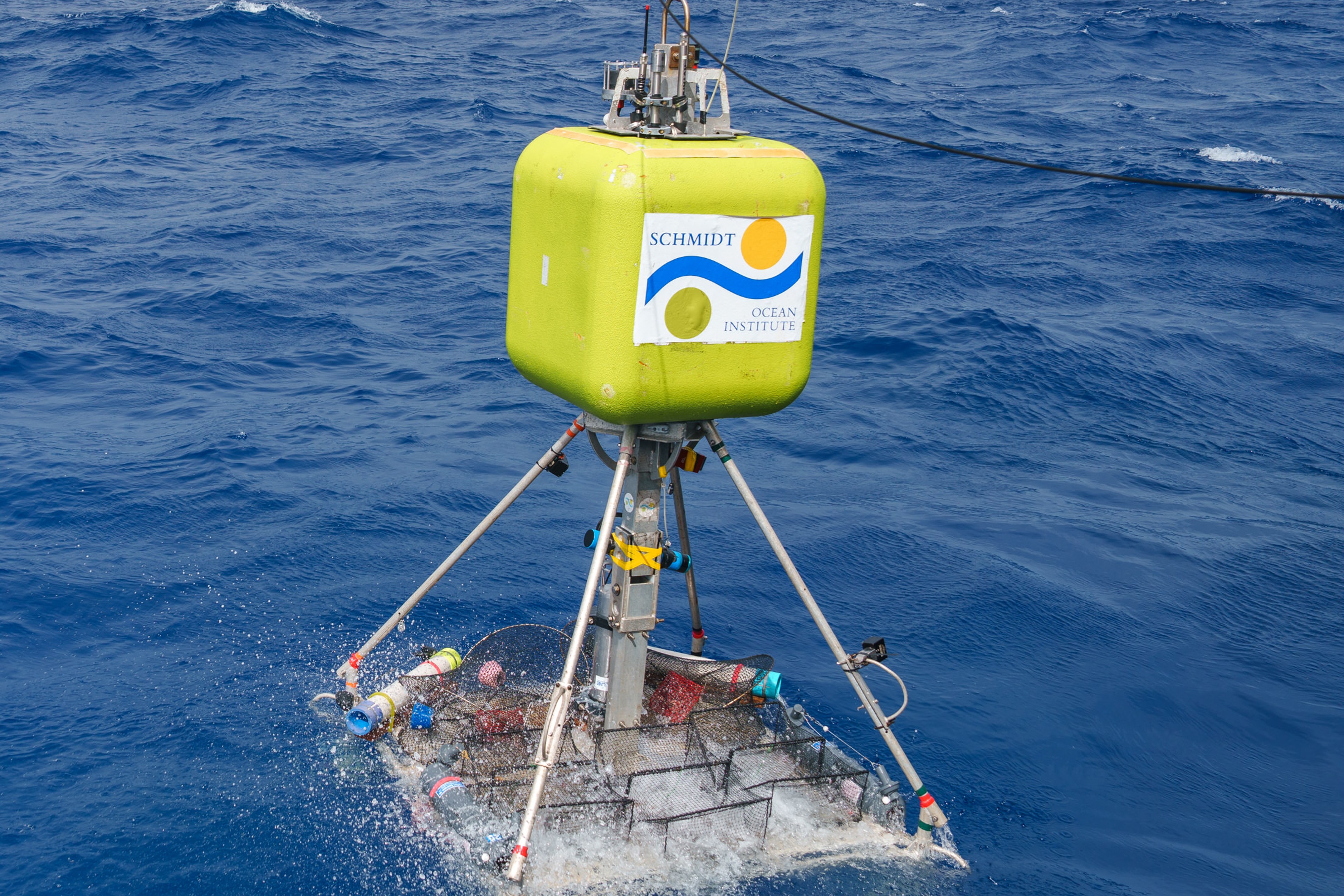 Lander with a yellow floatation square with the SOI logo on it, with a payload of traps being lowered into the water for deployment.