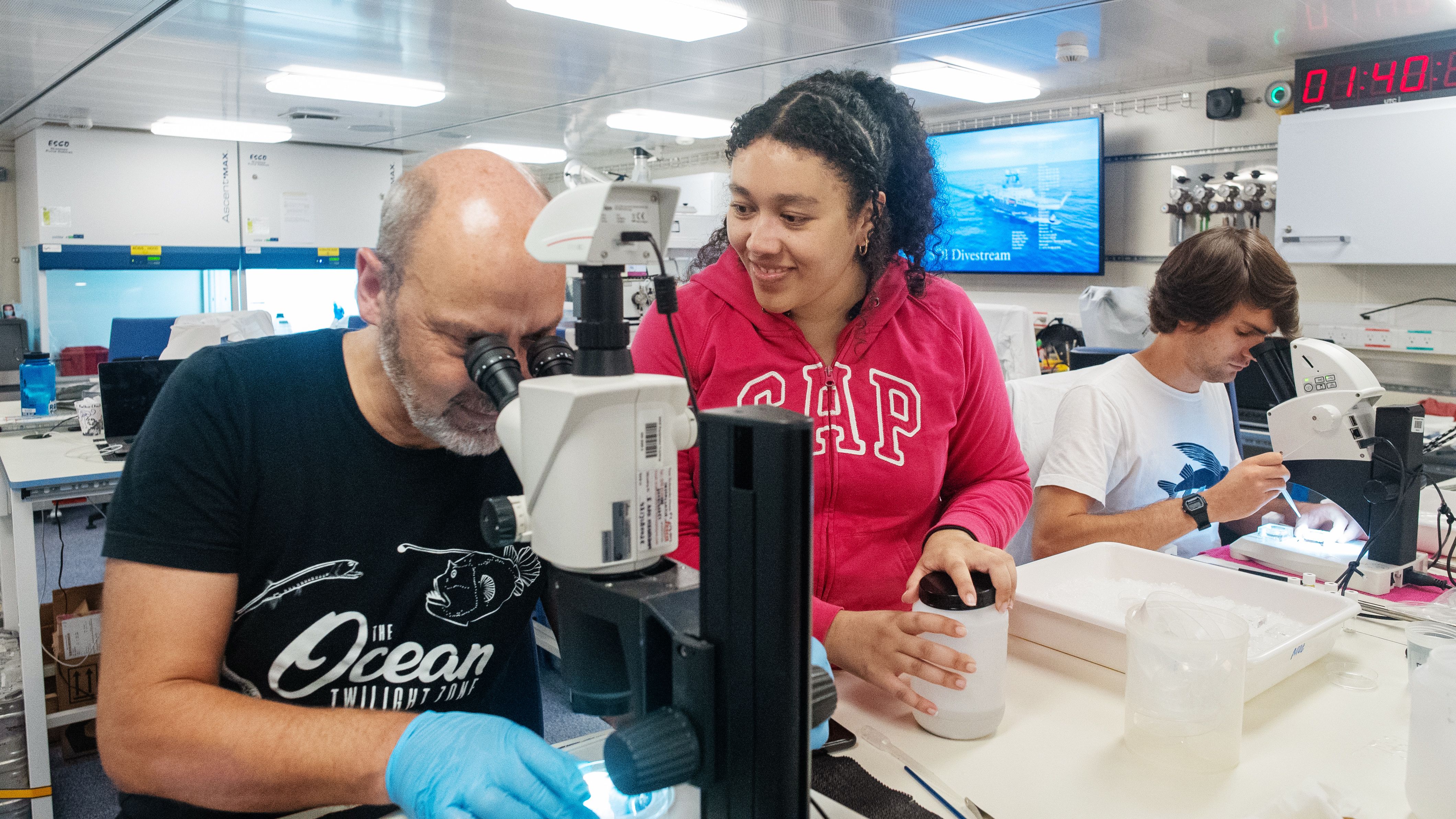 person looking through microscope while someone observes