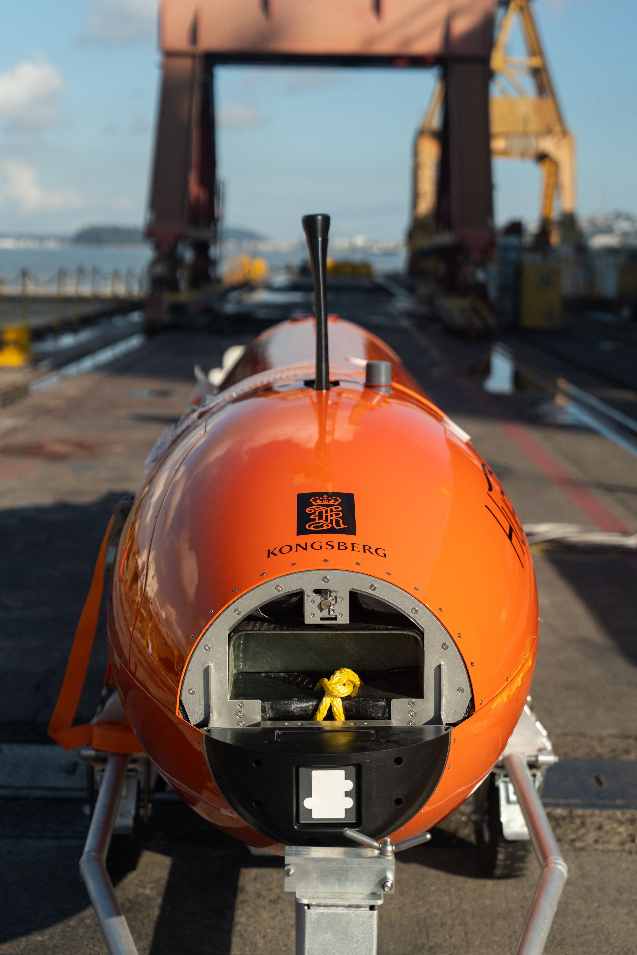 Head on view of the AUV in shipyard as it is being loaded onto the ship, highlighting the Kongsberg Discovery logo. 