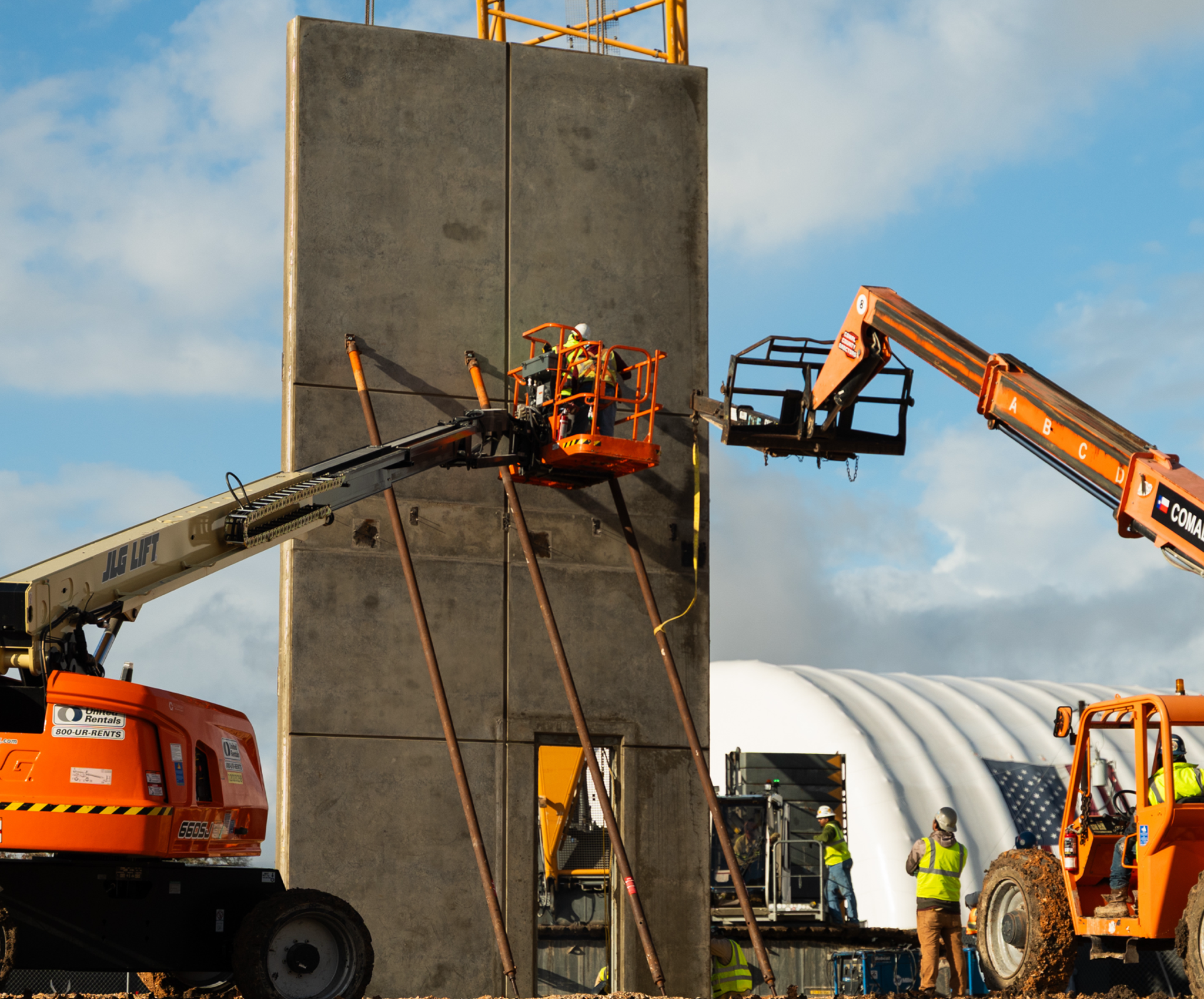 Workers on a lift beside a concrete wall at the construction site